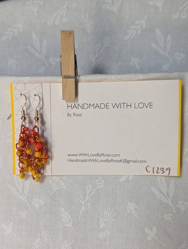 Handmade dangle earrings with 18 orange and yellow glass beads in six warm shades, linked with orange jump rings and rose gold-colored hooks.