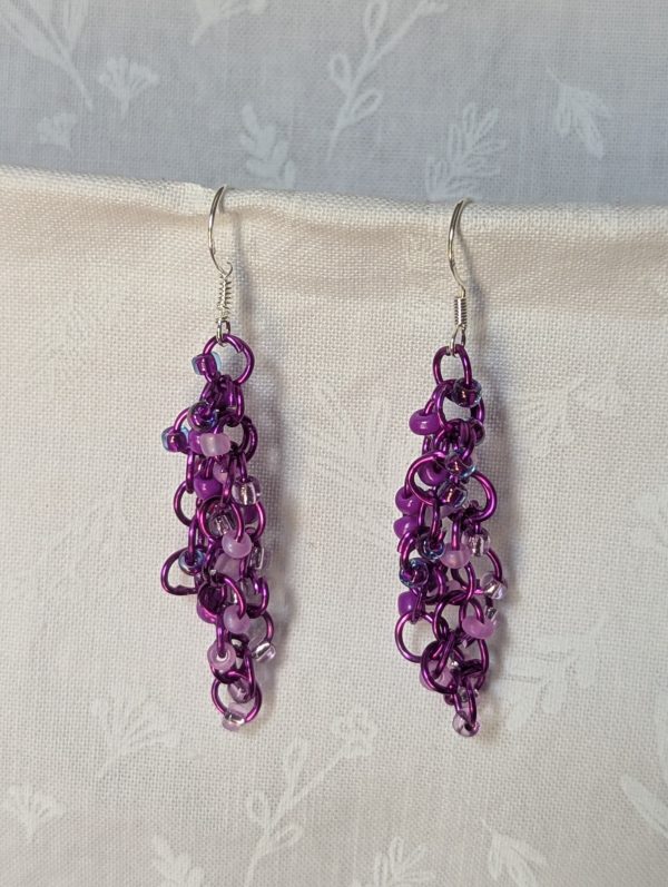Handmade purple dangle earrings with 24 glass beads in lilac, plum, lavender, and iridescent violet, attached with purple jump rings and sterling silver hooks.