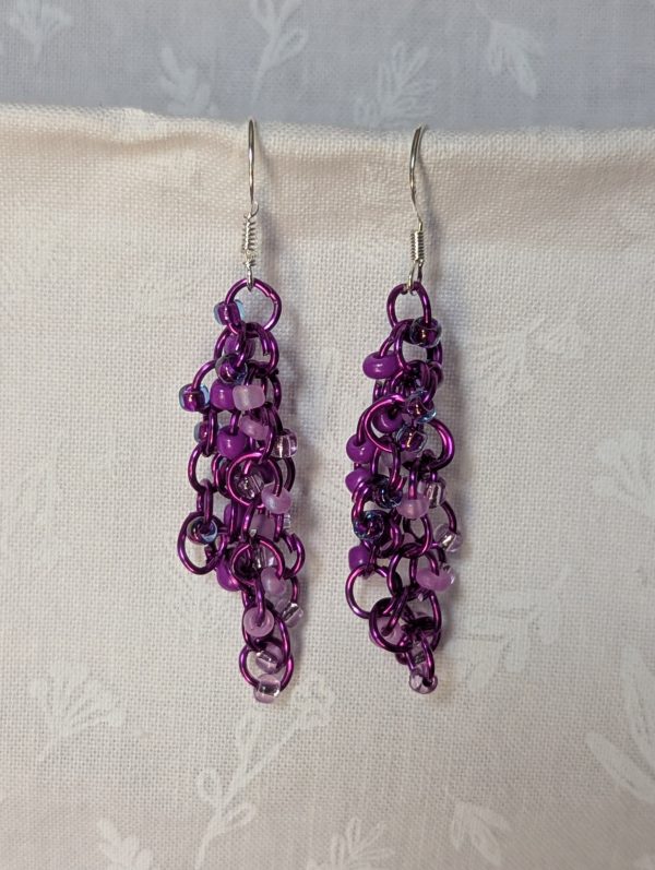Handmade purple dangle earrings with 24 glass beads in lilac, plum, lavender, and iridescent violet, attached with purple jump rings and sterling silver hooks.