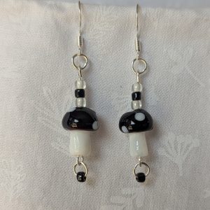 Handmade black mushroom earrings with glass toadstools, black and white seed beads, and sterling silver hooks.