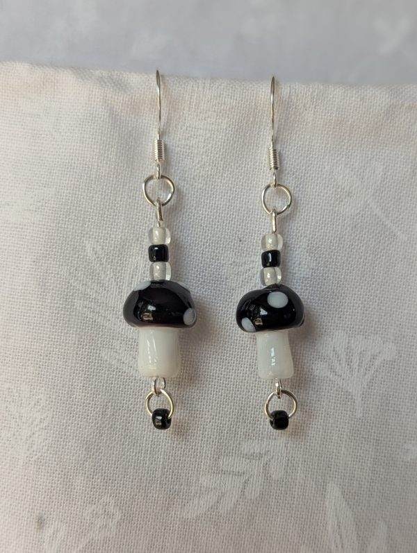 Handmade black mushroom earrings with glass toadstools, black and white seed beads, and sterling silver hooks.