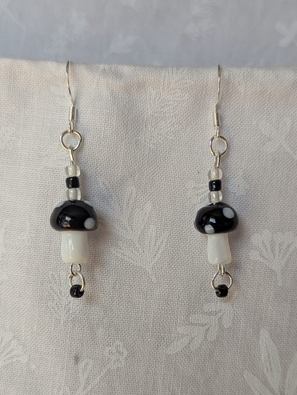 Handmade black mushroom earrings with glass toadstools, black and white seed beads, and sterling silver hooks.