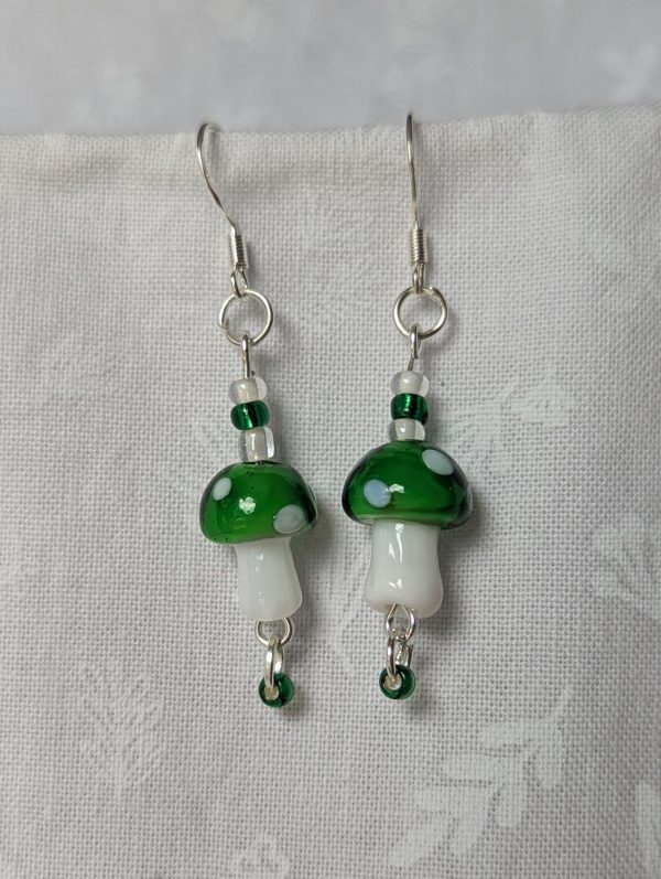 Handmade green mushroom earrings with glass toadstools, green and white seed beads, and sterling silver hooks.