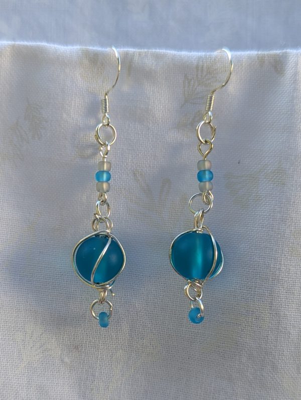 Handmade blue bead earrings with silver wire wrapping, blue and blue-gray seed beads, silver jump rings, and sterling silver hooks.