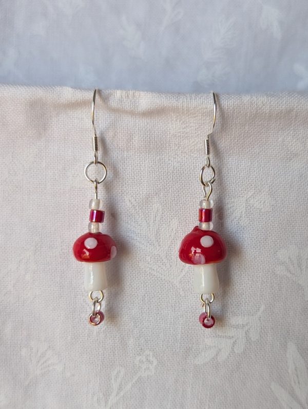 Handmade red mushroom earrings with glass toadstools, red and white seed beads, and sterling silver hooks.