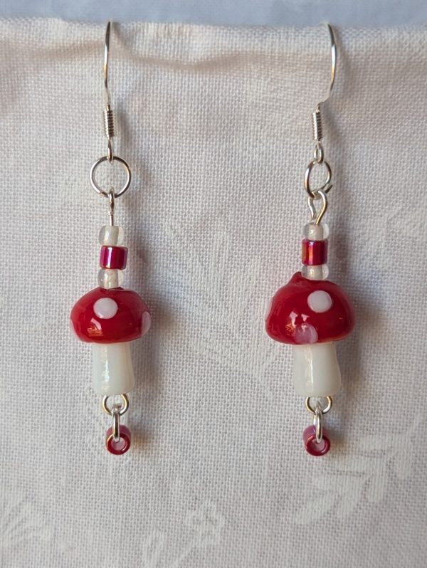 Handmade red mushroom earrings with glass toadstools, red and white seed beads, and sterling silver hooks.