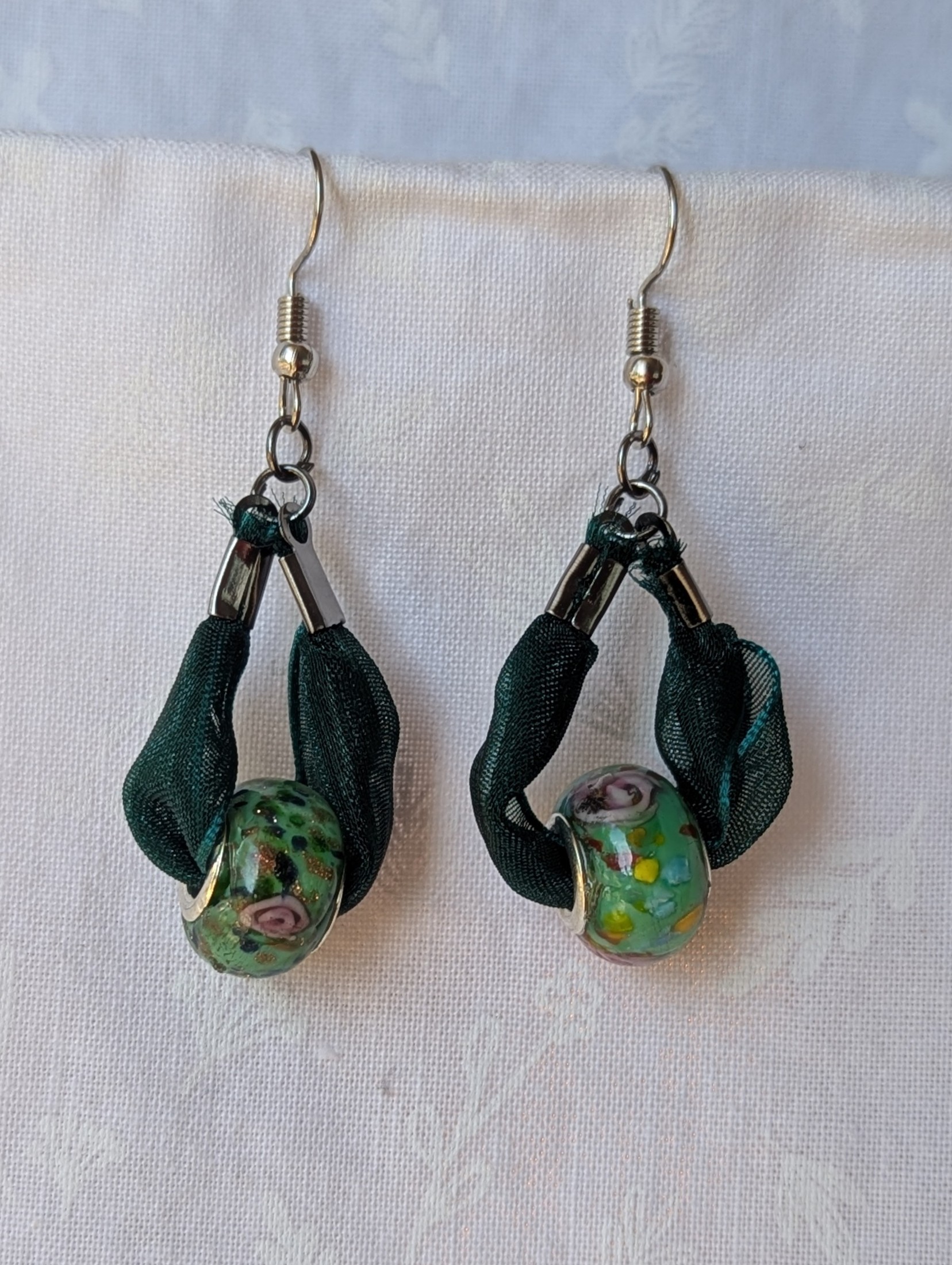 Handmade green ribbon earrings featuring floral glass beads with tungsten metal accents and steel hooks.