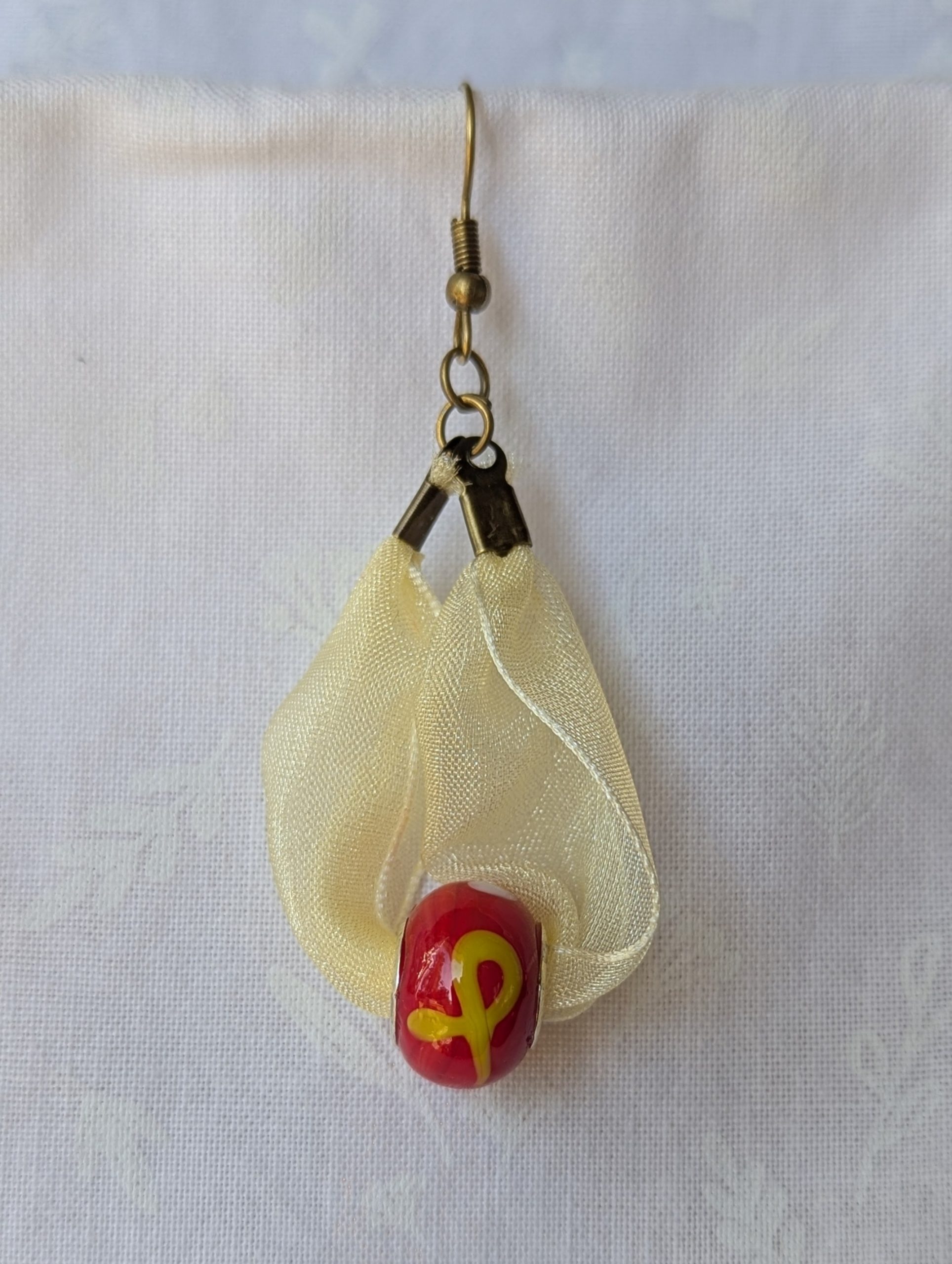 Handmade pale yellow ribbon earrings featuring bright red glass beads with yellow accents and hung from bronze-colored hooks.