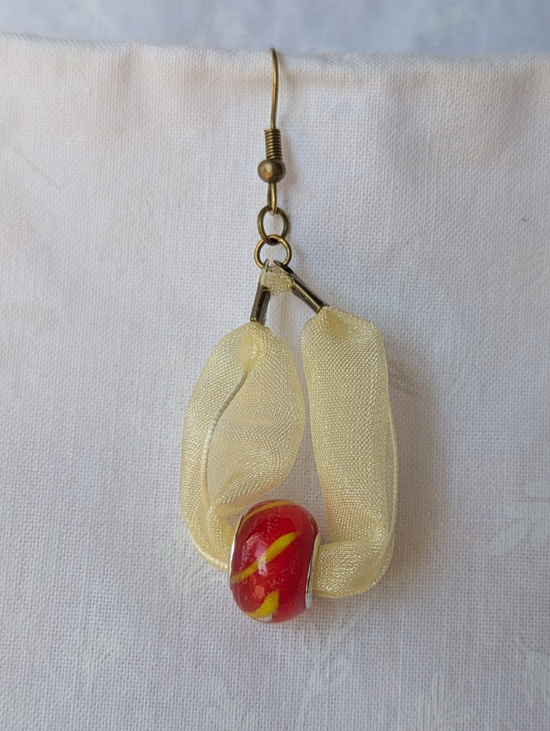 Handmade pale yellow ribbon earrings featuring bright red glass beads with yellow accents and hung from bronze-colored hooks.