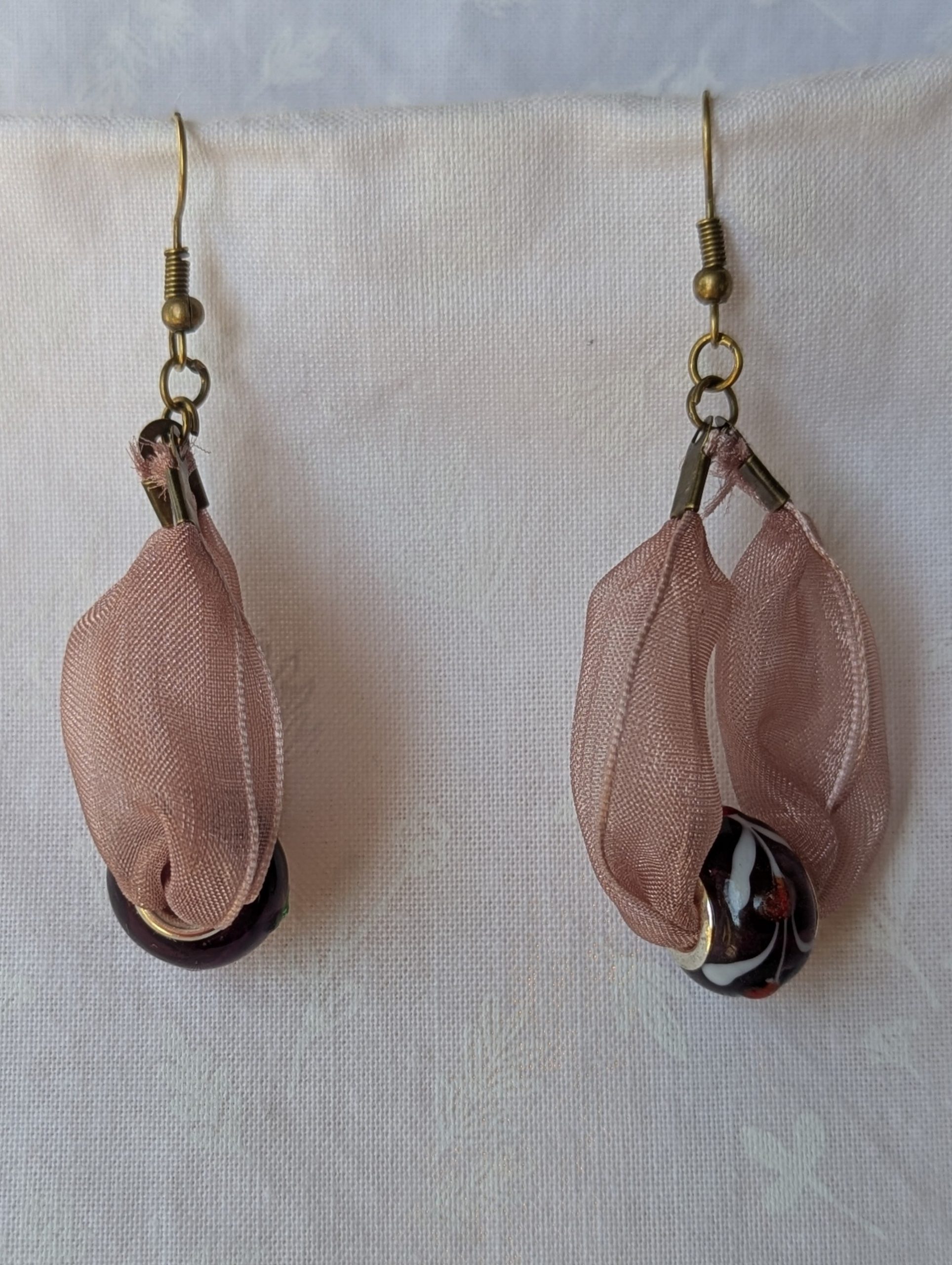Handmade pink and black ribbon earrings featuring black beads with white and red accents and hung from bronze-colored hooks.