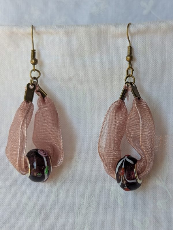 Handmade pink and black ribbon earrings featuring black beads with white and red accents and hung from bronze-colored hooks.