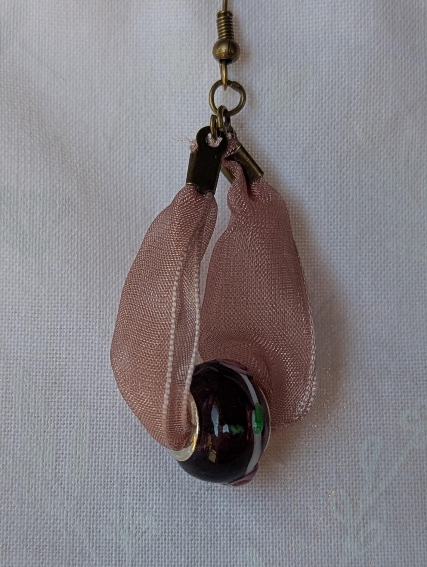 Handmade pink and black ribbon earrings featuring black beads with white and red accents and hung from bronze-colored hooks.