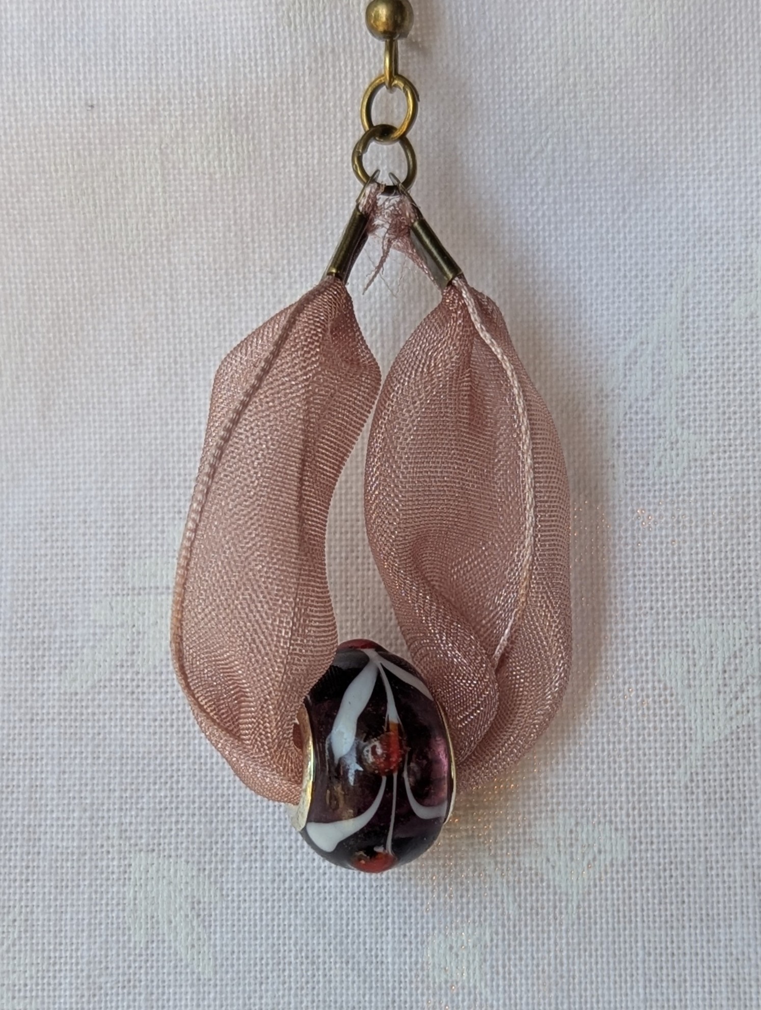 Handmade pink and black ribbon earrings featuring black beads with white and red accents and hung from bronze-colored hooks.
