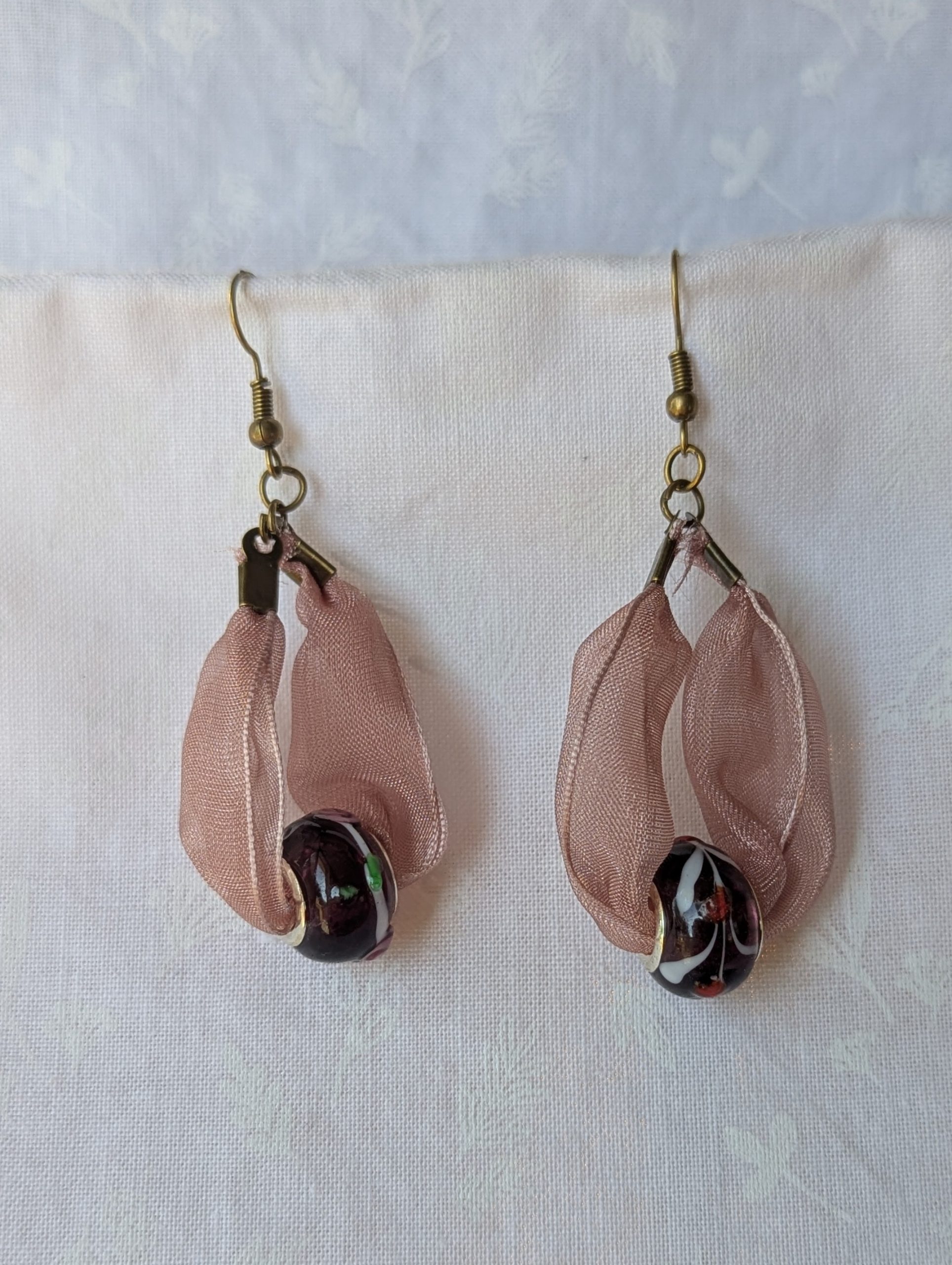 Handmade pink and black ribbon earrings featuring black beads with white and red accents and hung from bronze-colored hooks.