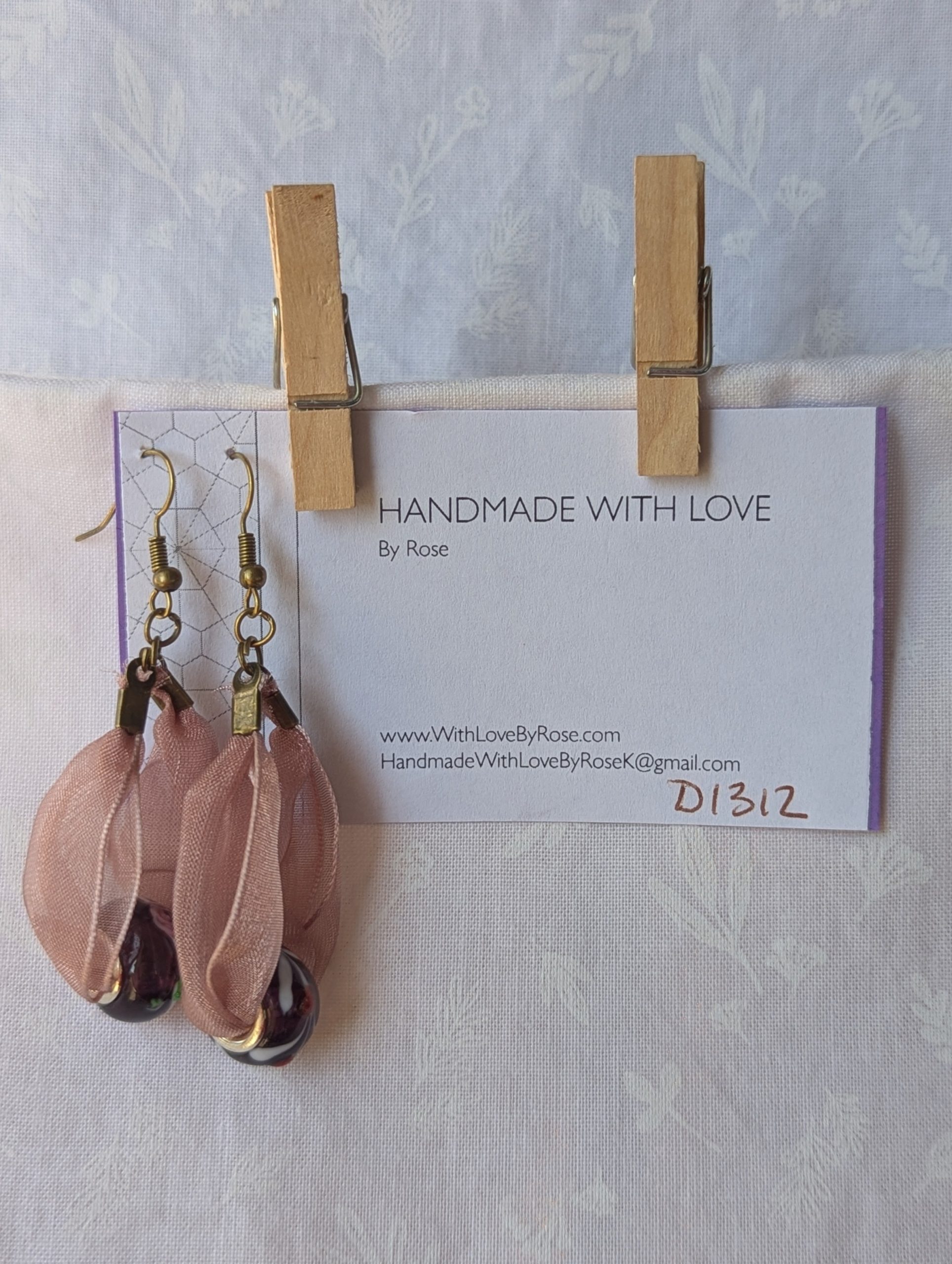 Handmade pink and black ribbon earrings featuring black beads with white and red accents and hung from bronze-colored hooks.