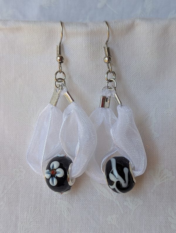 Handmade white and black ribbon earrings featuring black beads with white accents and hung from steel-colored hooks.