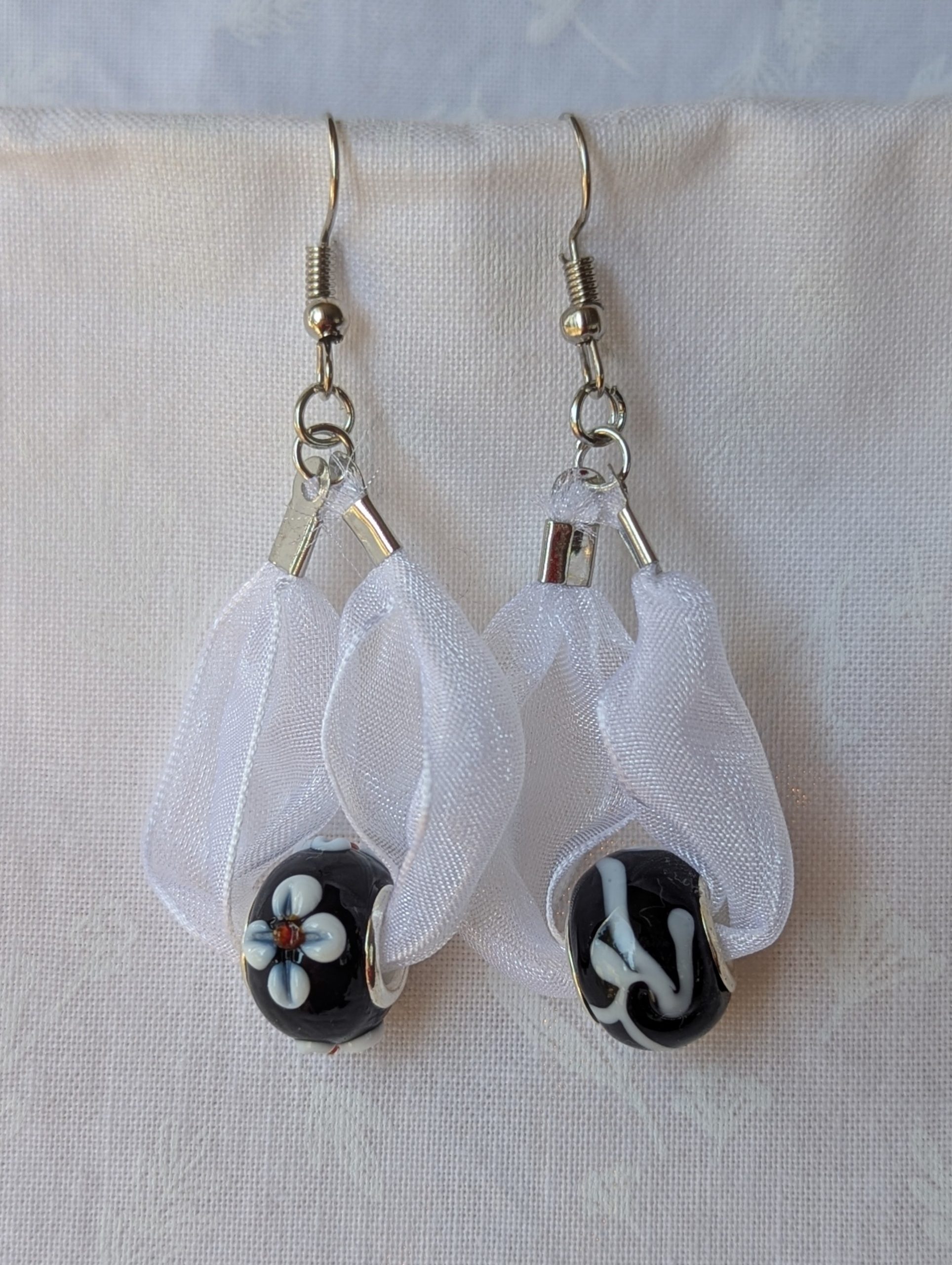 Handmade white and black ribbon earrings featuring black beads with white accents and hung from steel-colored hooks.