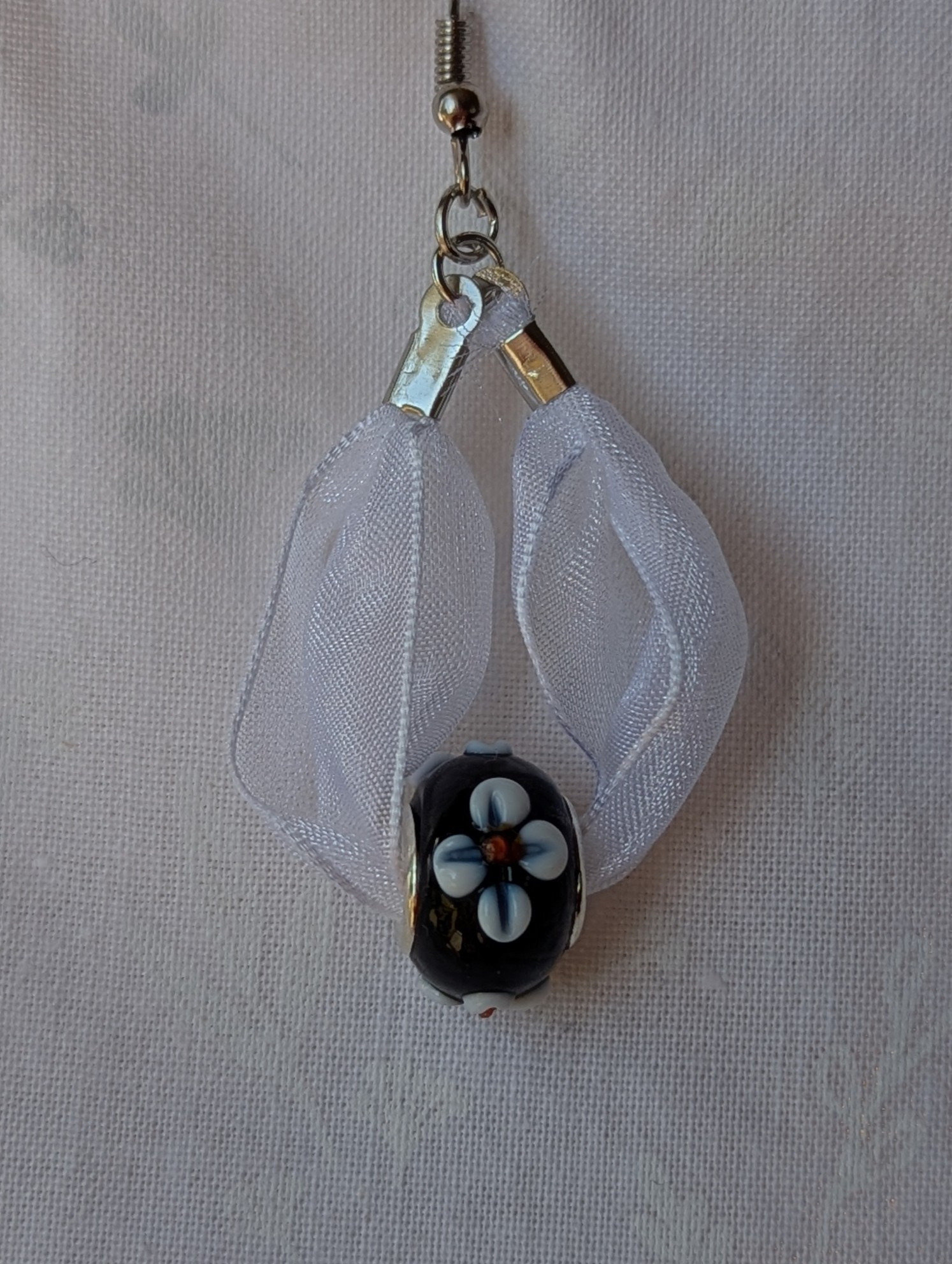 Handmade white and black ribbon earrings featuring black beads with white accents and hung from steel-colored hooks.