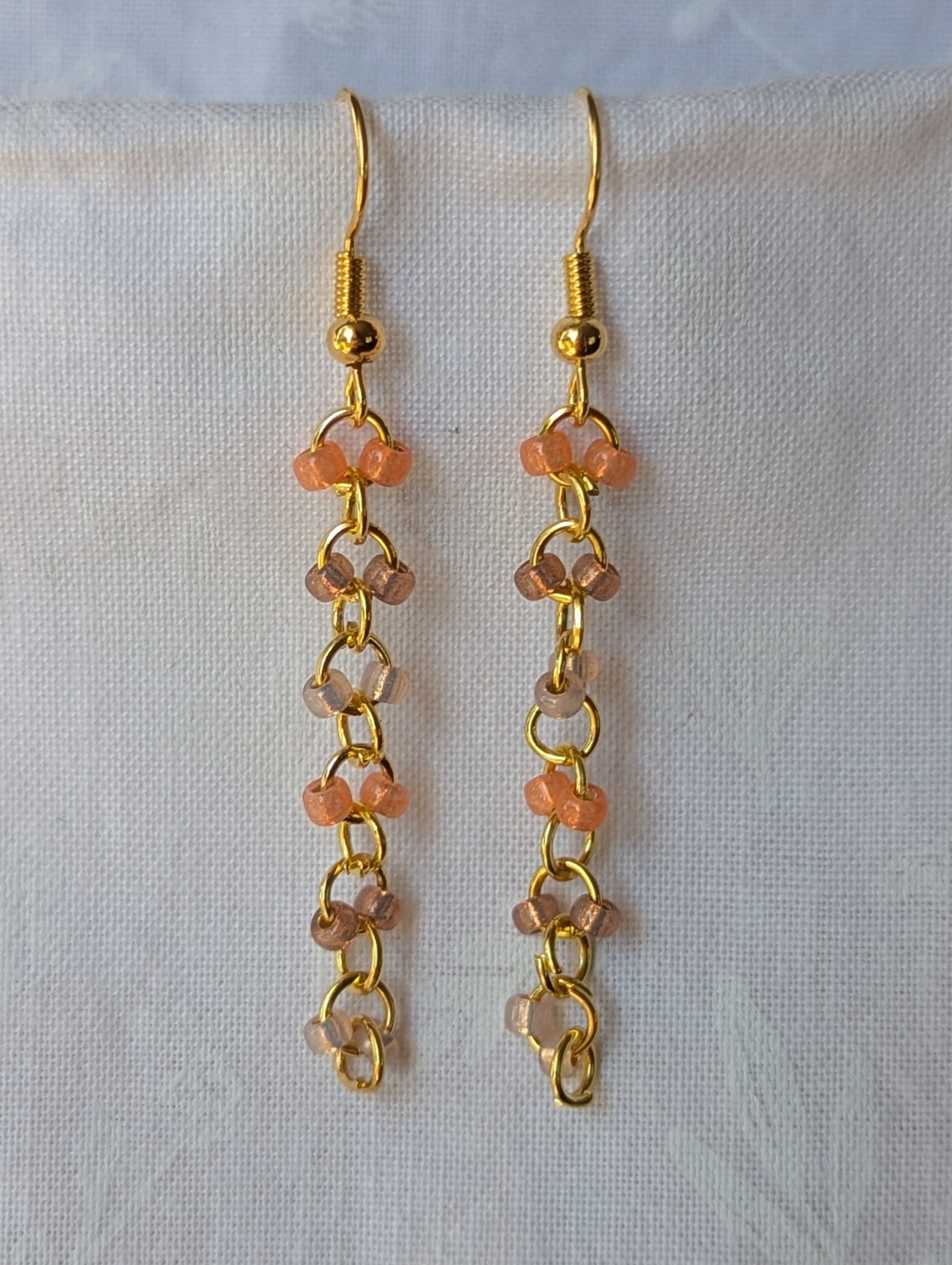 Handmade gold beaded earrings with 12 peach and champagne glass beads connected by gold-colored metal and matching hooks.