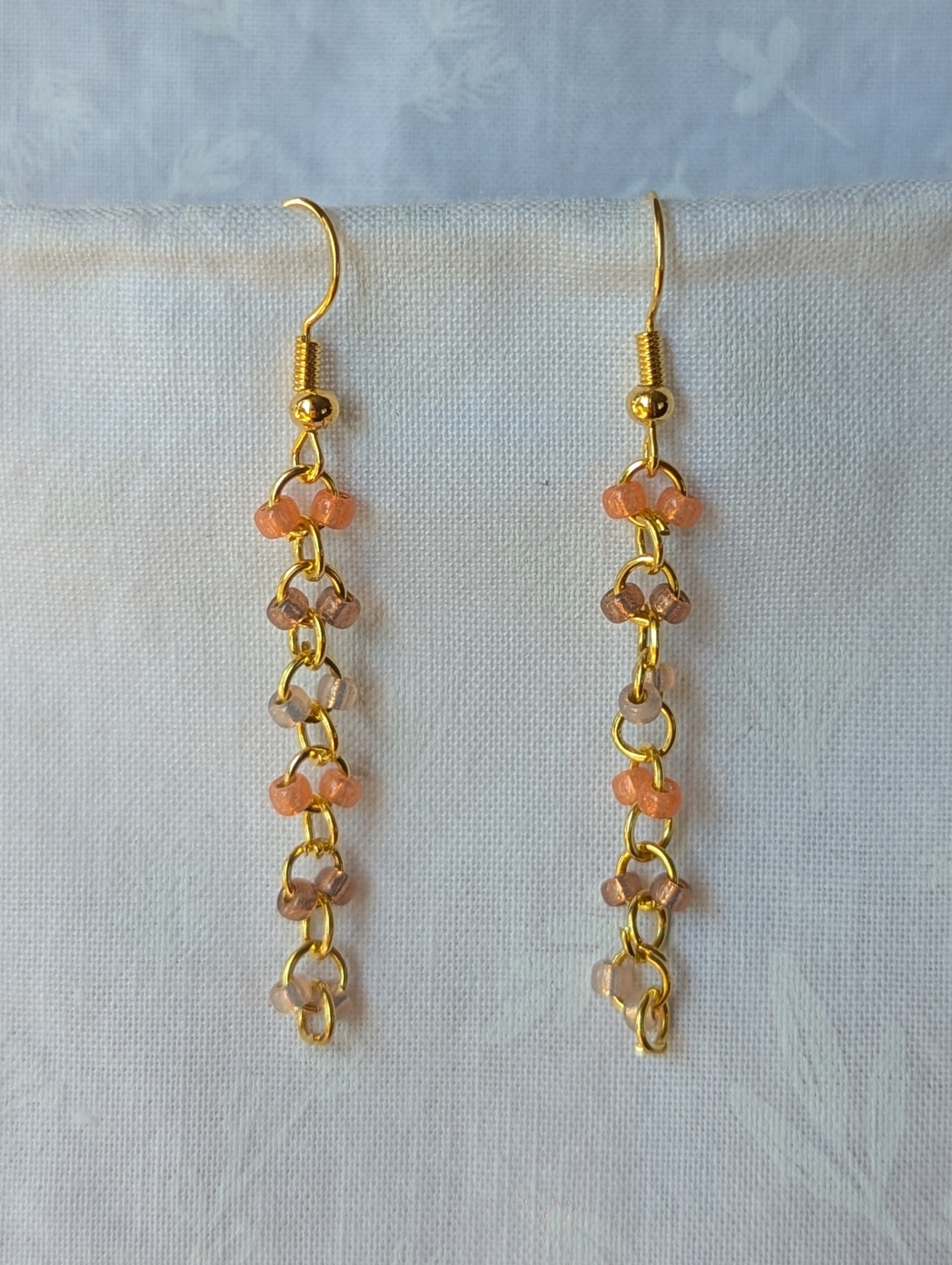 Handmade gold beaded earrings with 12 peach and champagne glass beads connected by gold-colored metal and matching hooks.