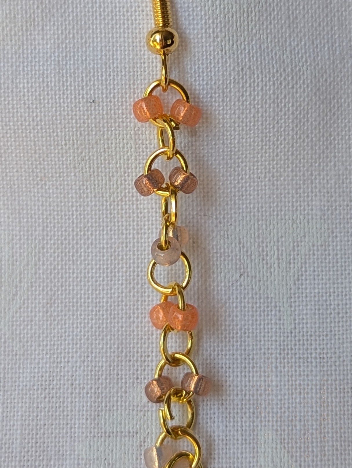 Handmade gold beaded earrings with 12 peach and champagne glass beads connected by gold-colored metal and matching hooks.