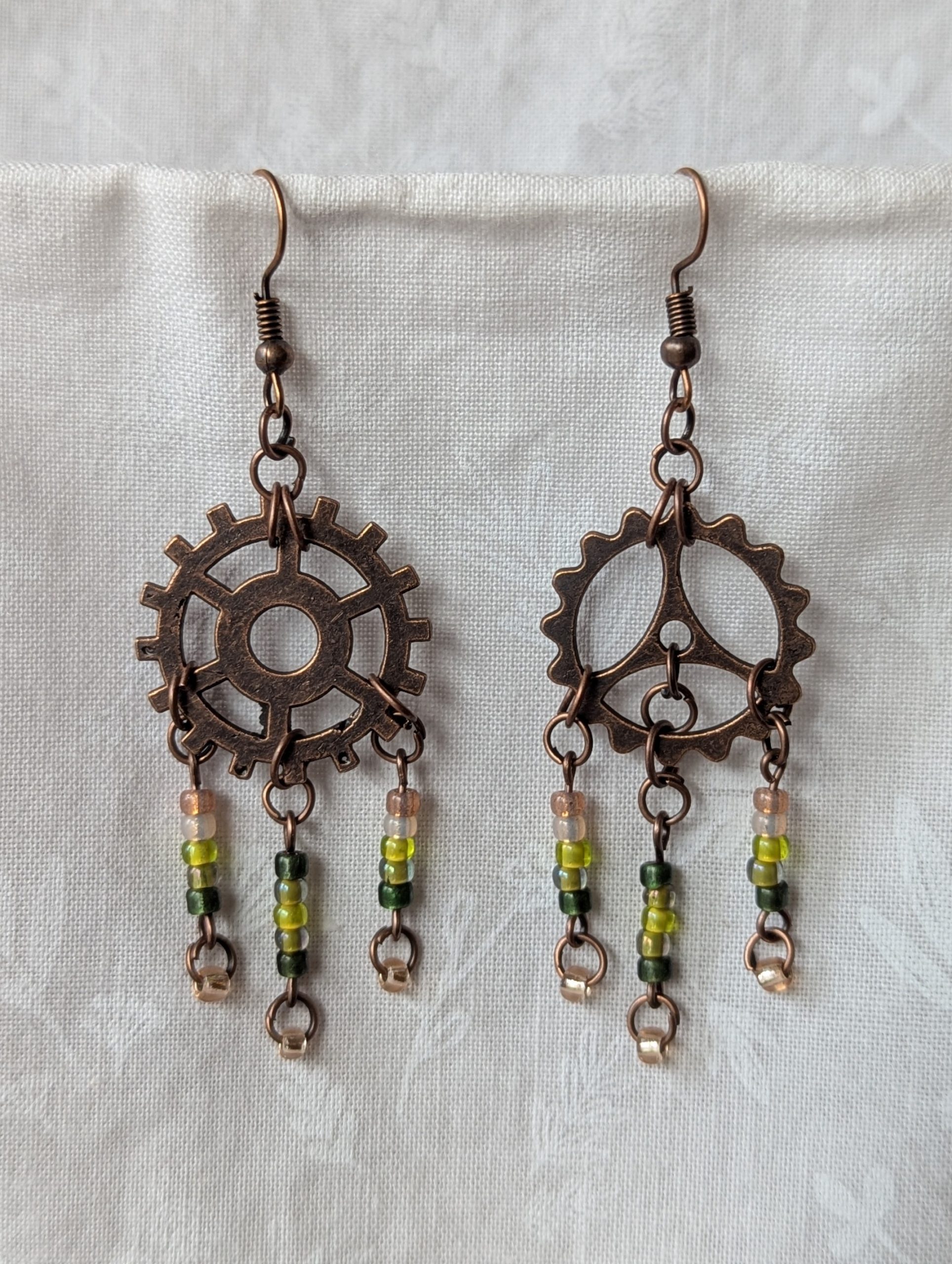 Handmade bronze gear steampunk earrings with green and brown glass beads, asymmetrical steampunk design, and antique bronze hooks.