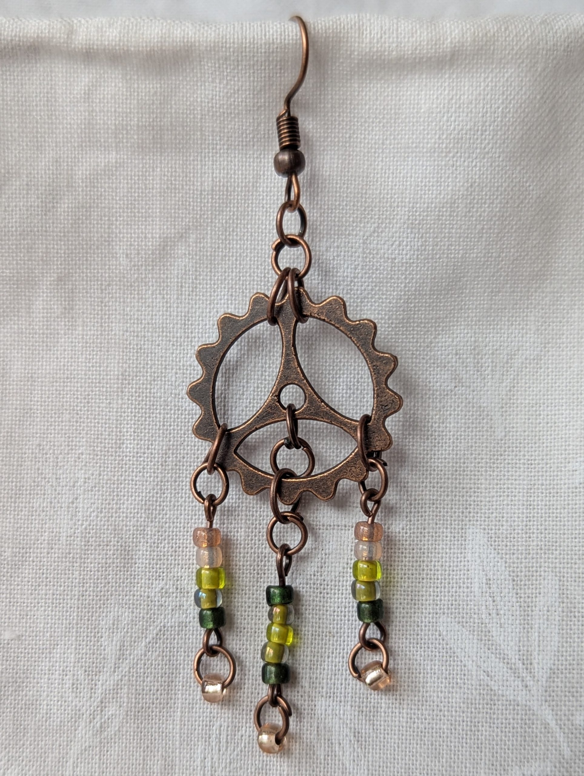 Handmade bronze gear steampunk earrings with green and brown glass beads, asymmetrical steampunk design, and antique bronze hooks.