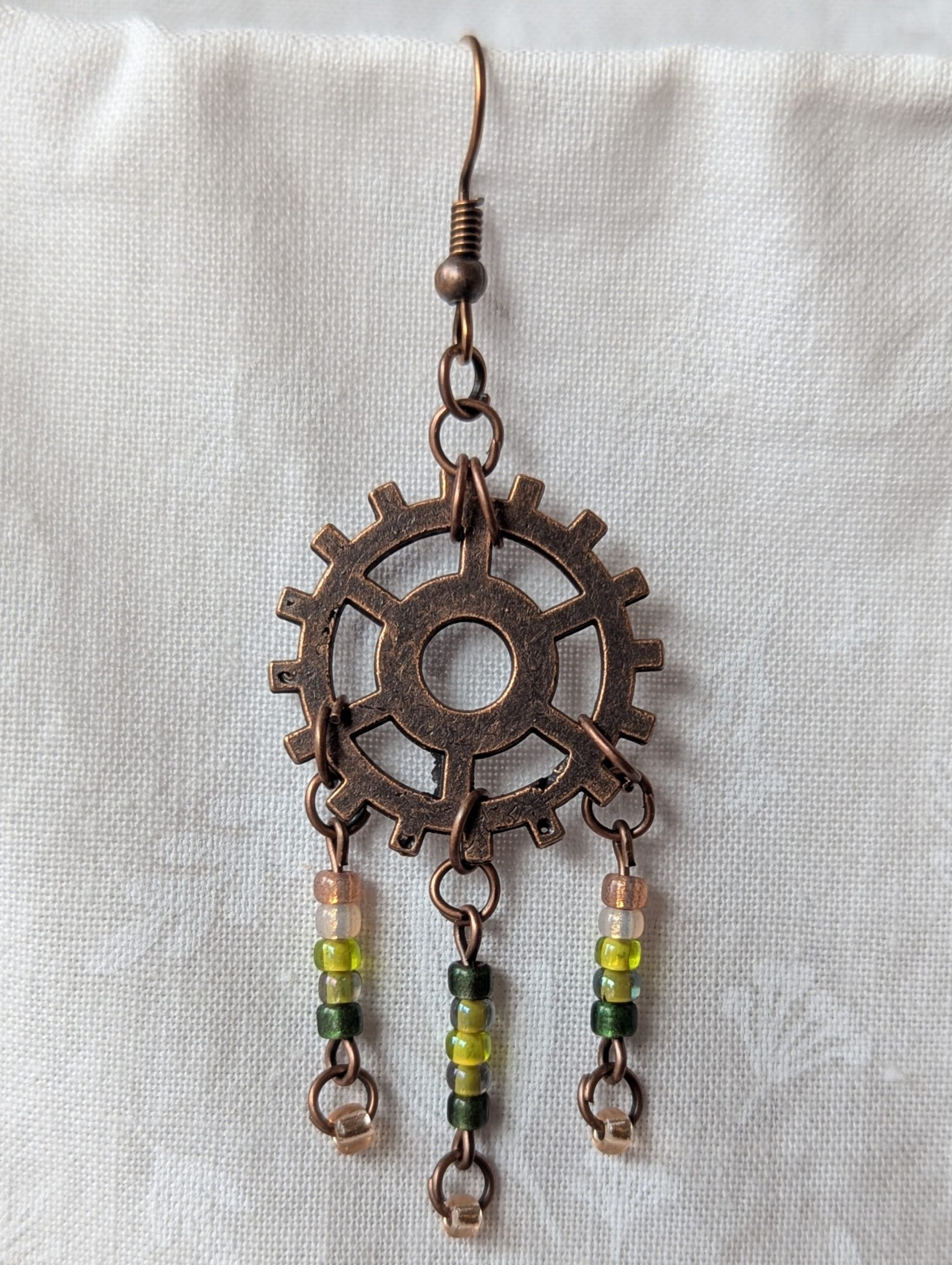 Handmade bronze gear steampunk earrings with green and brown glass beads, asymmetrical steampunk design, and antique bronze hooks.