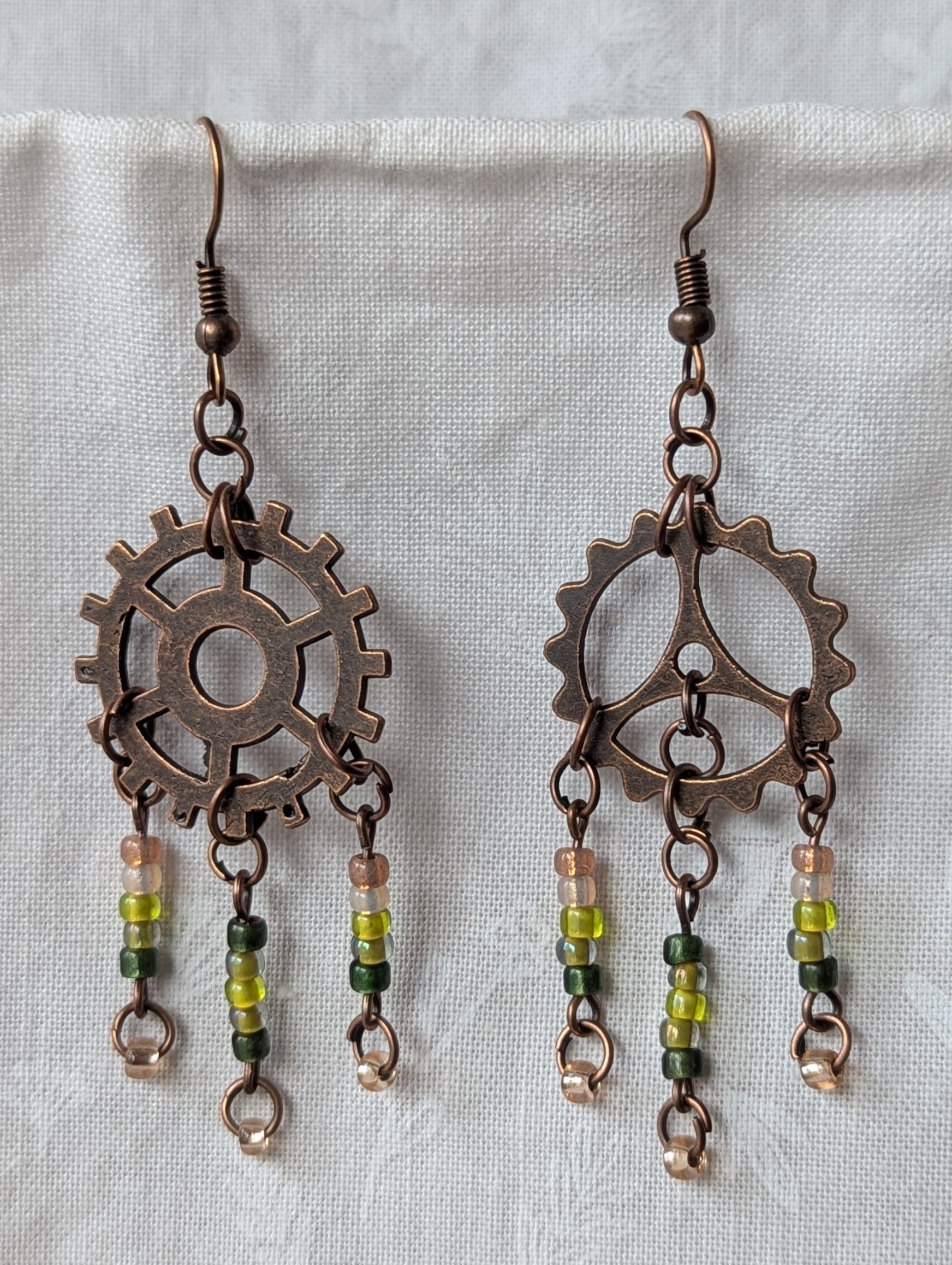 Handmade bronze gear steampunk earrings with green and brown glass beads, asymmetrical steampunk design, and antique bronze hooks.