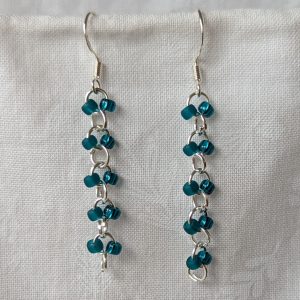 Handmade teal glass earrings featuring frosted and silver-lined teal beads connected with silver jump rings and sterling silver hooks.