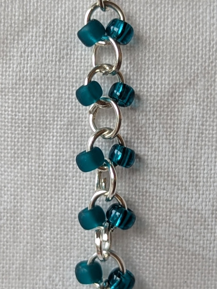 Handmade teal glass earrings featuring frosted and silver-lined teal beads connected with silver jump rings and sterling silver hooks.