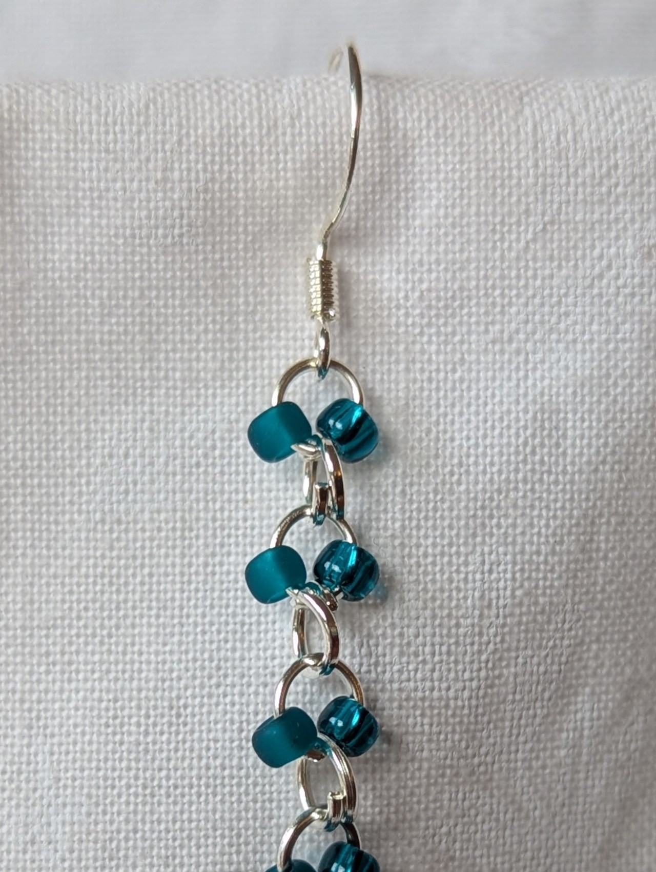 Handmade teal glass earrings featuring frosted and silver-lined teal beads connected with silver jump rings and sterling silver hooks.