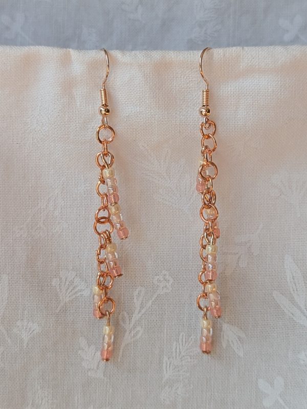 Handmade blush cream beaded earrings featuring pale pink and cream glass beads in four shades, linked with copper jump rings and rose-gold hooks.