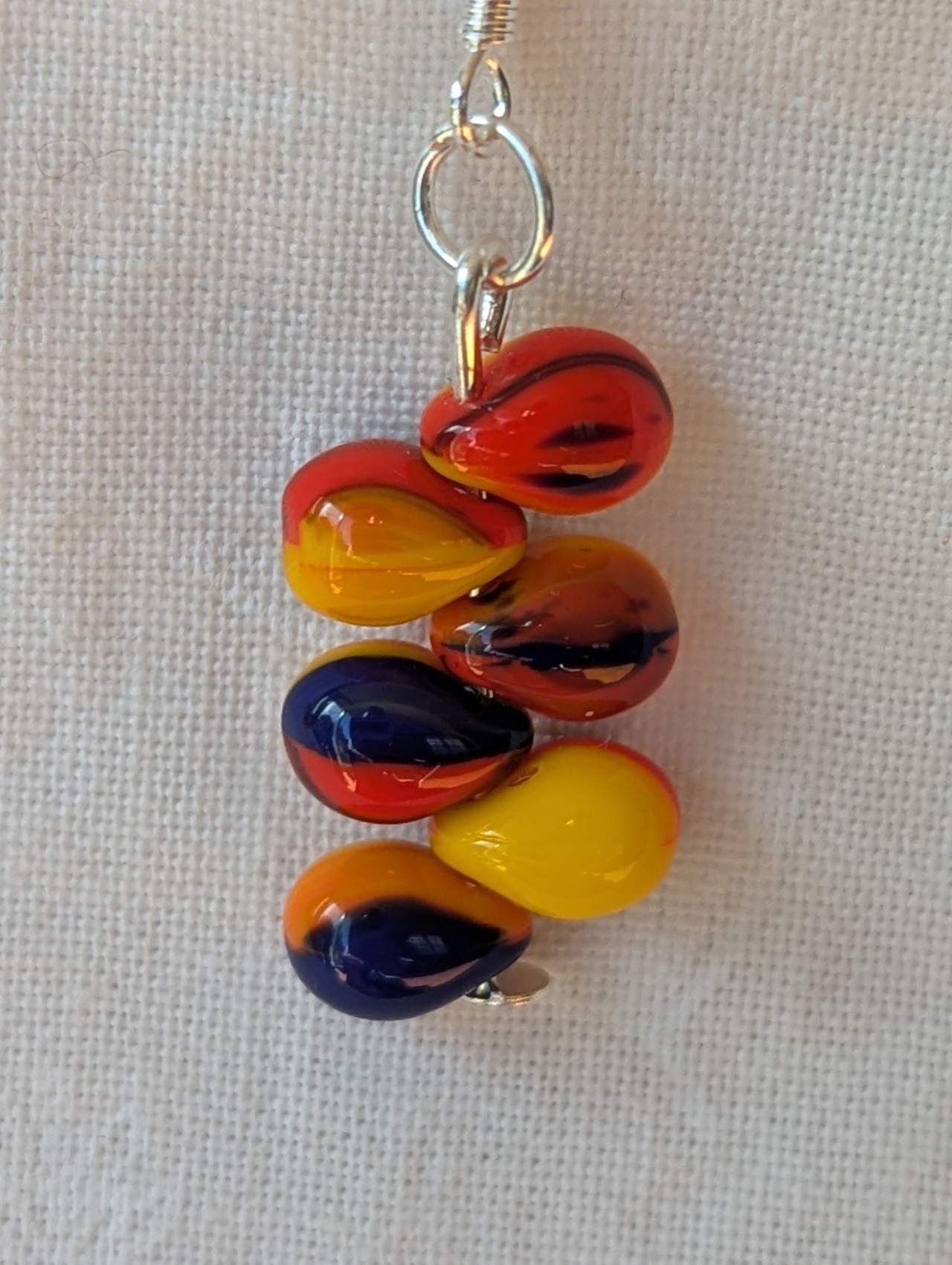 Handmade fireburst glass bead earrings featuring yellow, red, and blue teardrop beads on silver pins with sterling silver hooks.