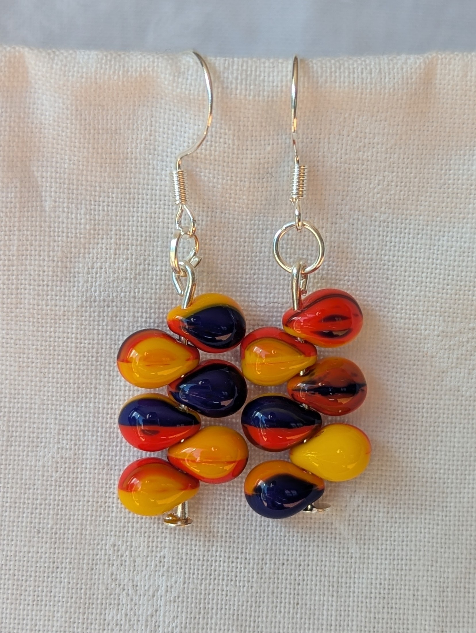 Handmade fireburst glass bead earrings featuring yellow, red, and blue teardrop beads on silver pins with sterling silver hooks.