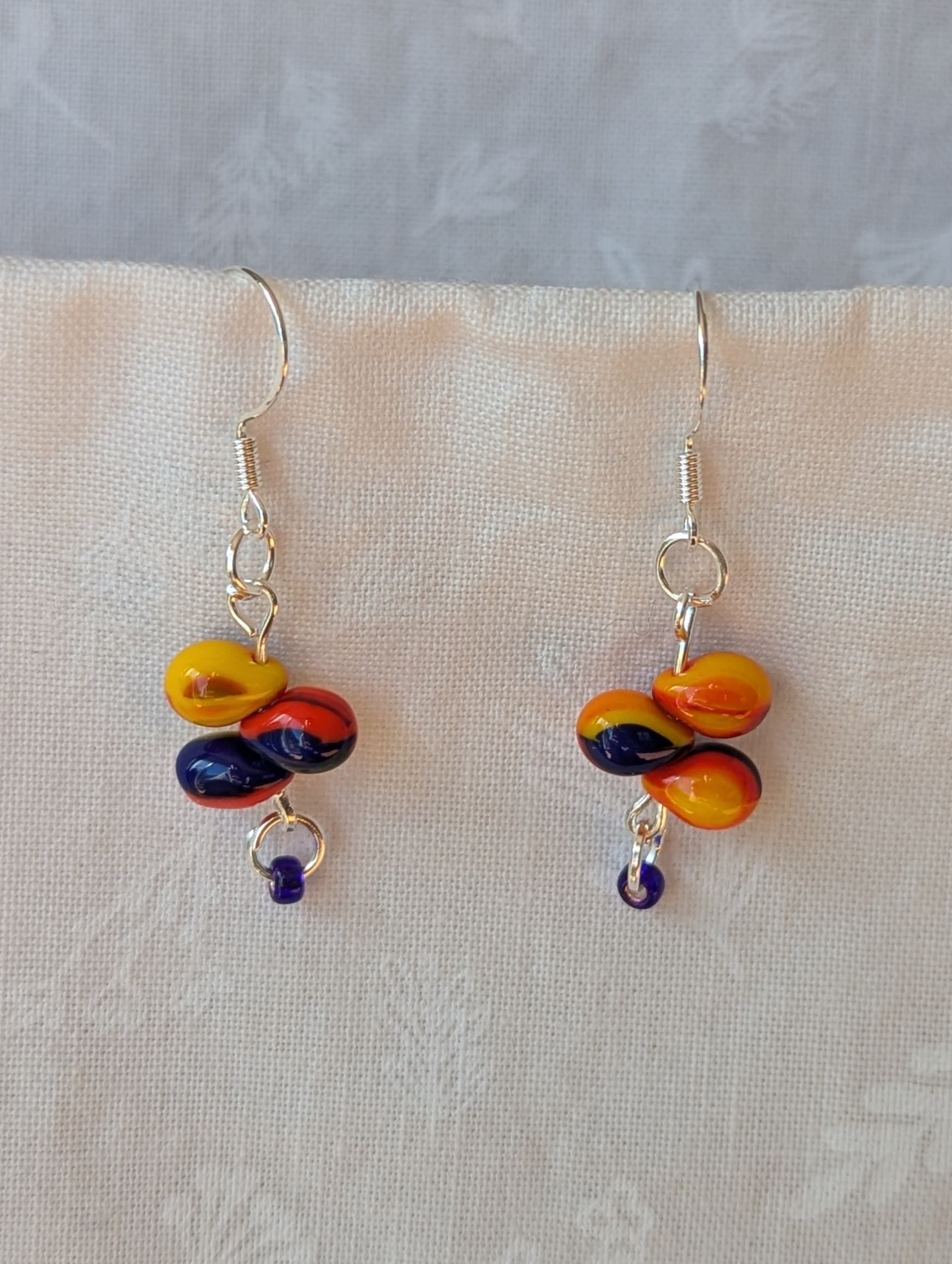 Handmade fireburst trio teardrop glass bead earrings featuring yellow, red, and blue teardrop beads on silver pins with sterling silver hooks.