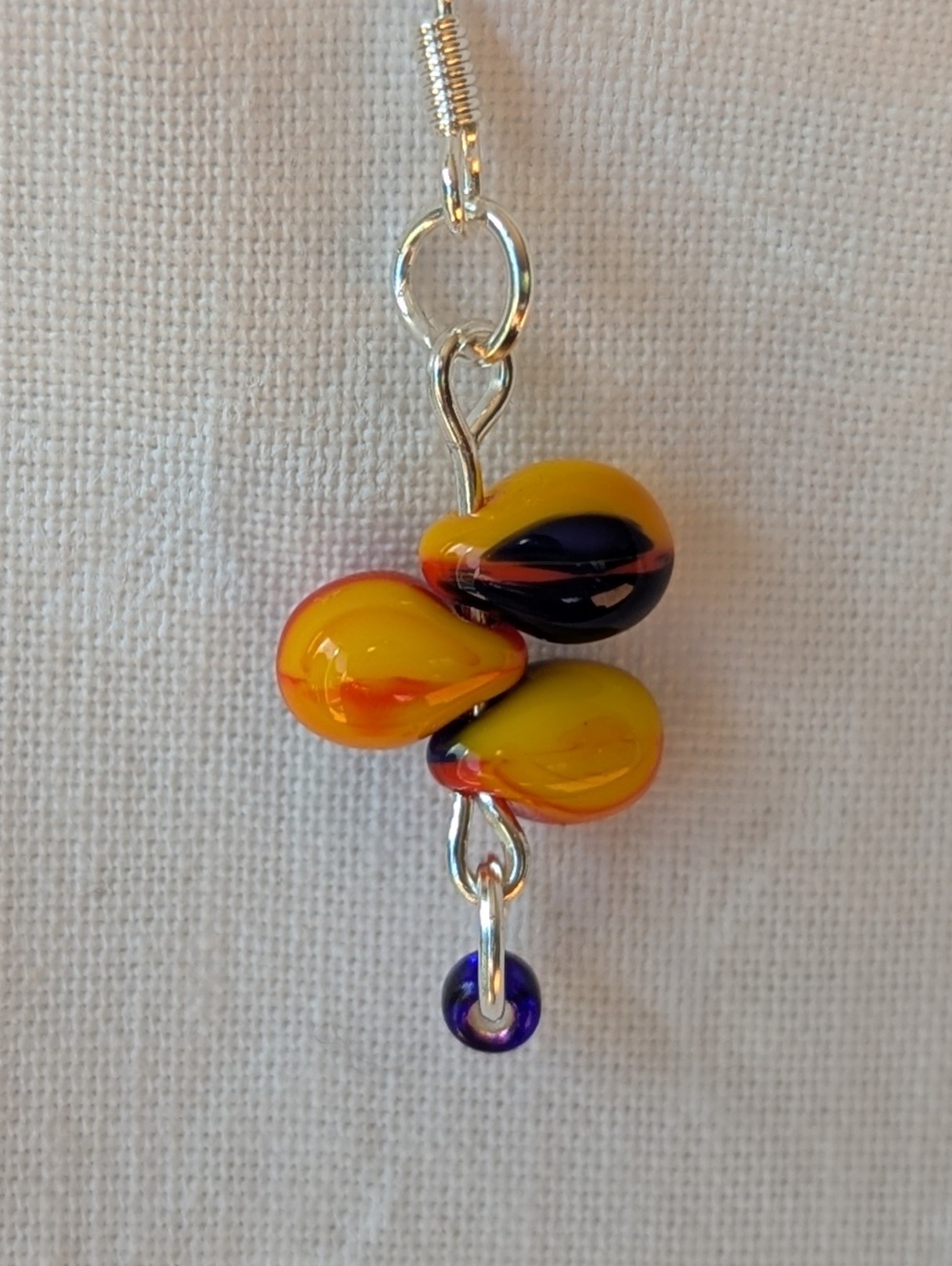 Handmade fireburst trio teardrop glass bead earrings featuring yellow, red, and blue teardrop beads on silver pins with sterling silver hooks.