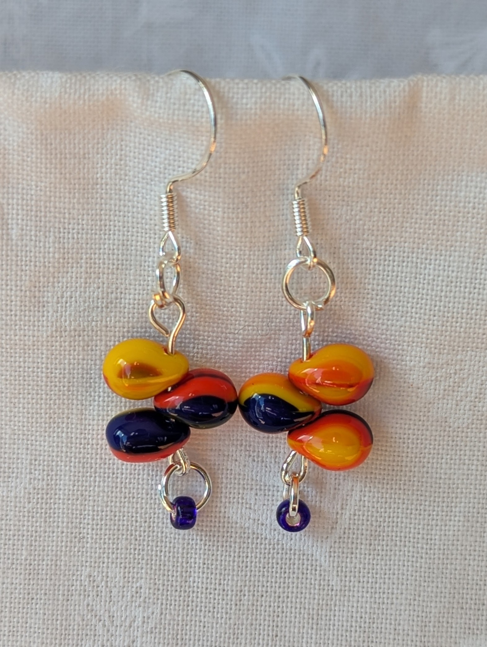 Handmade fireburst trio teardrop glass bead earrings featuring yellow, red, and blue teardrop beads on silver pins with sterling silver hooks.