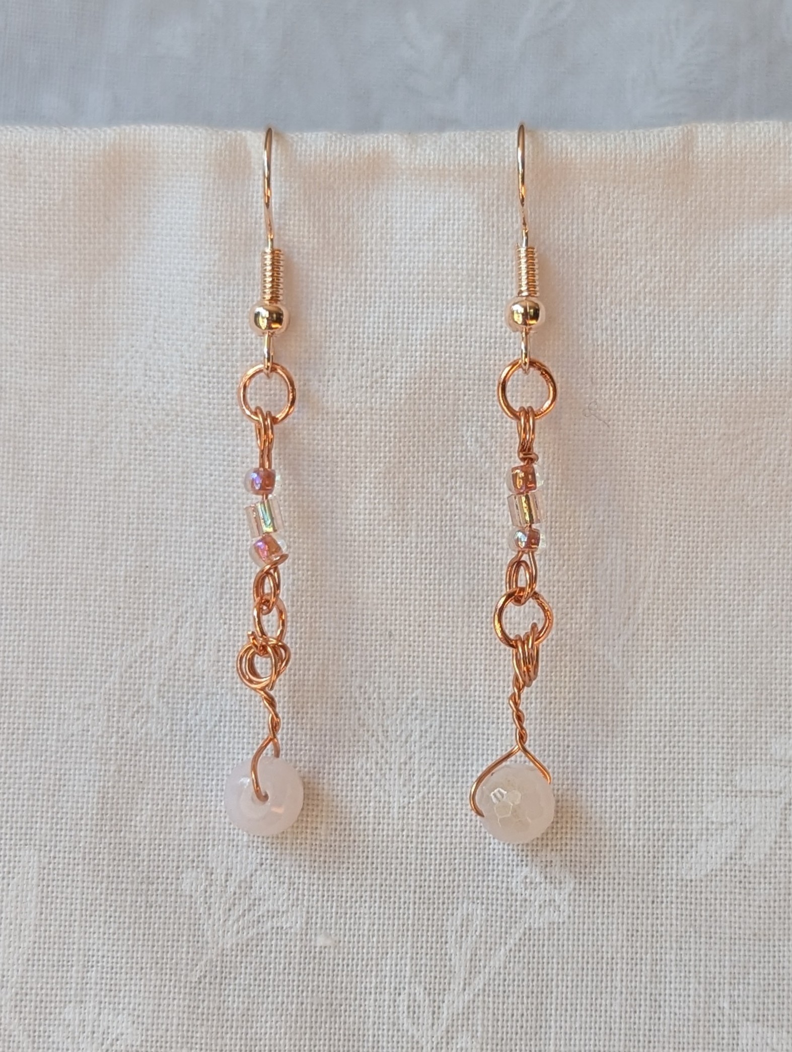 Handmade blush moonlight earrings with white Czech cut beads and pink seed beads wrapped in copper wire on rose-gold hooks.