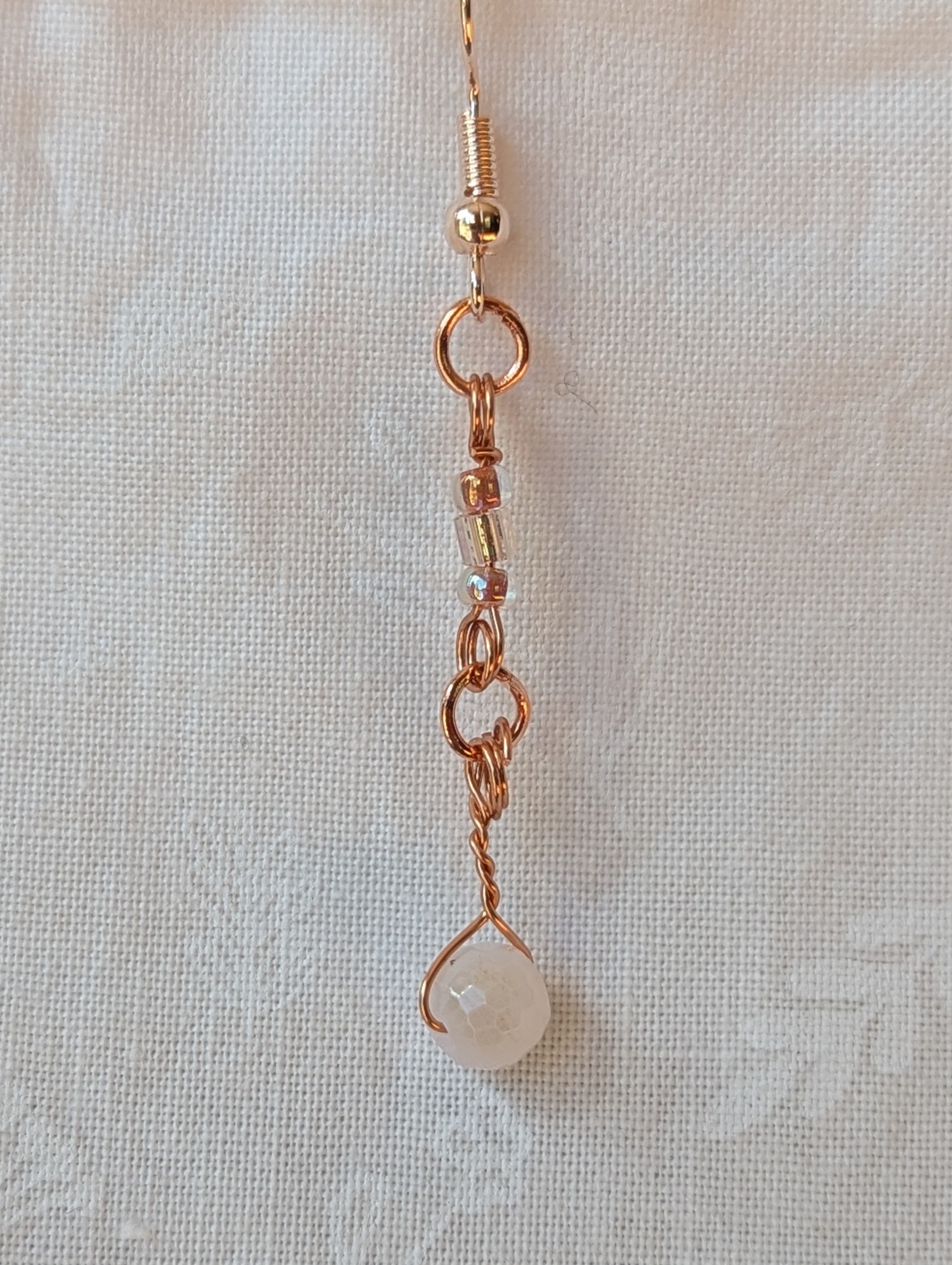 Handmade blush moonlight earrings with white Czech cut beads and pink seed beads wrapped in copper wire on rose-gold hooks.