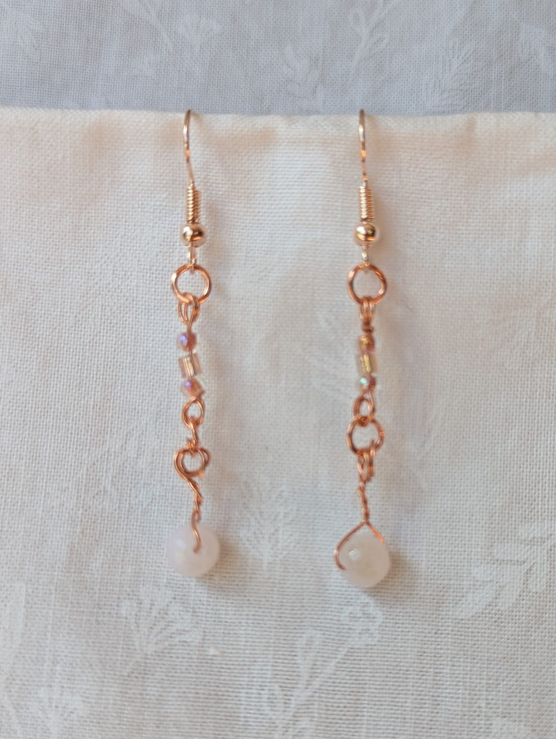 Handmade blush moonlight earrings with white Czech cut beads and pink seed beads wrapped in copper wire on rose-gold hooks.