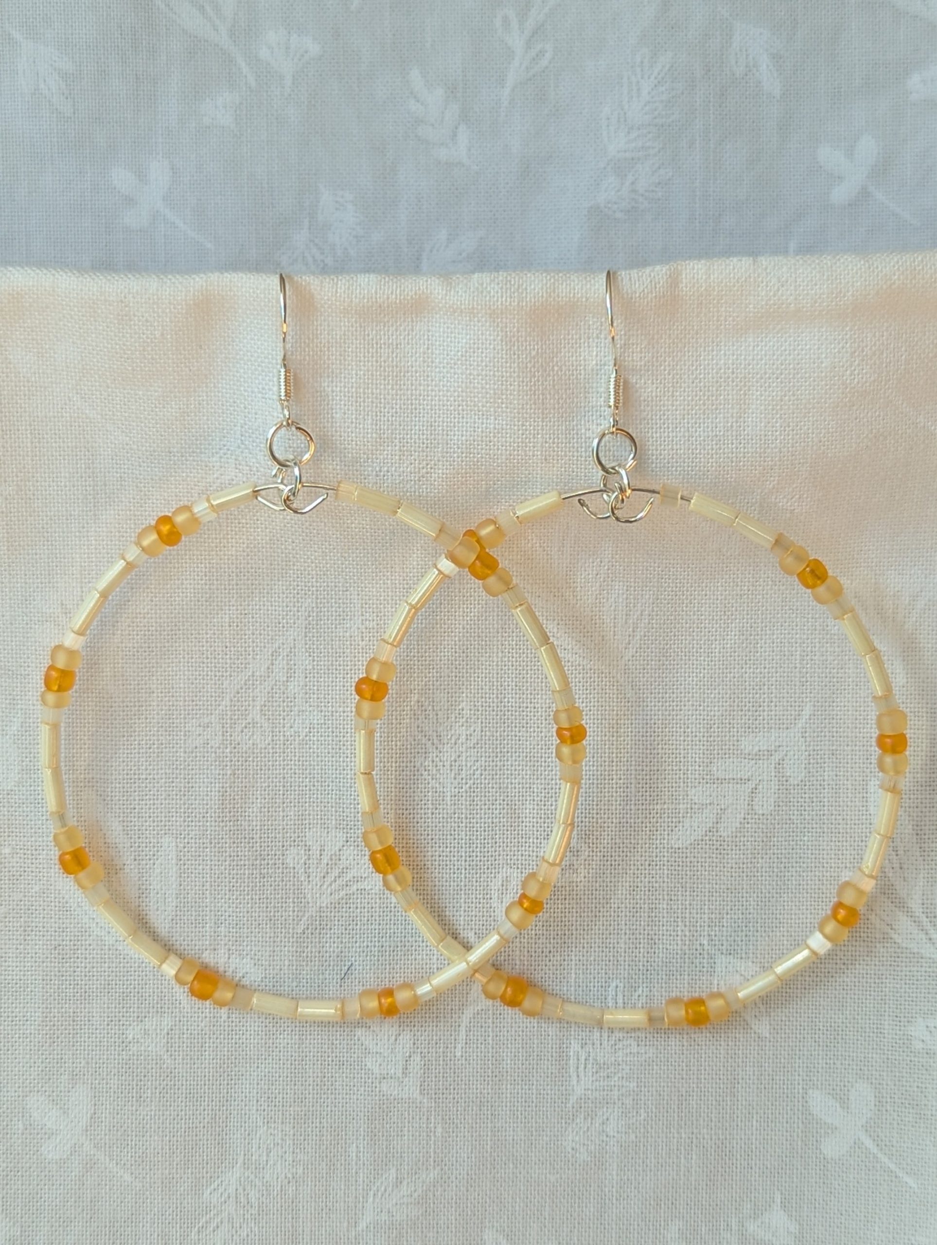 Handmade cream and sunshine yellow/orange beaded hoop earrings with glass beads on silver-plated memory wire and sterling silver hooks.
