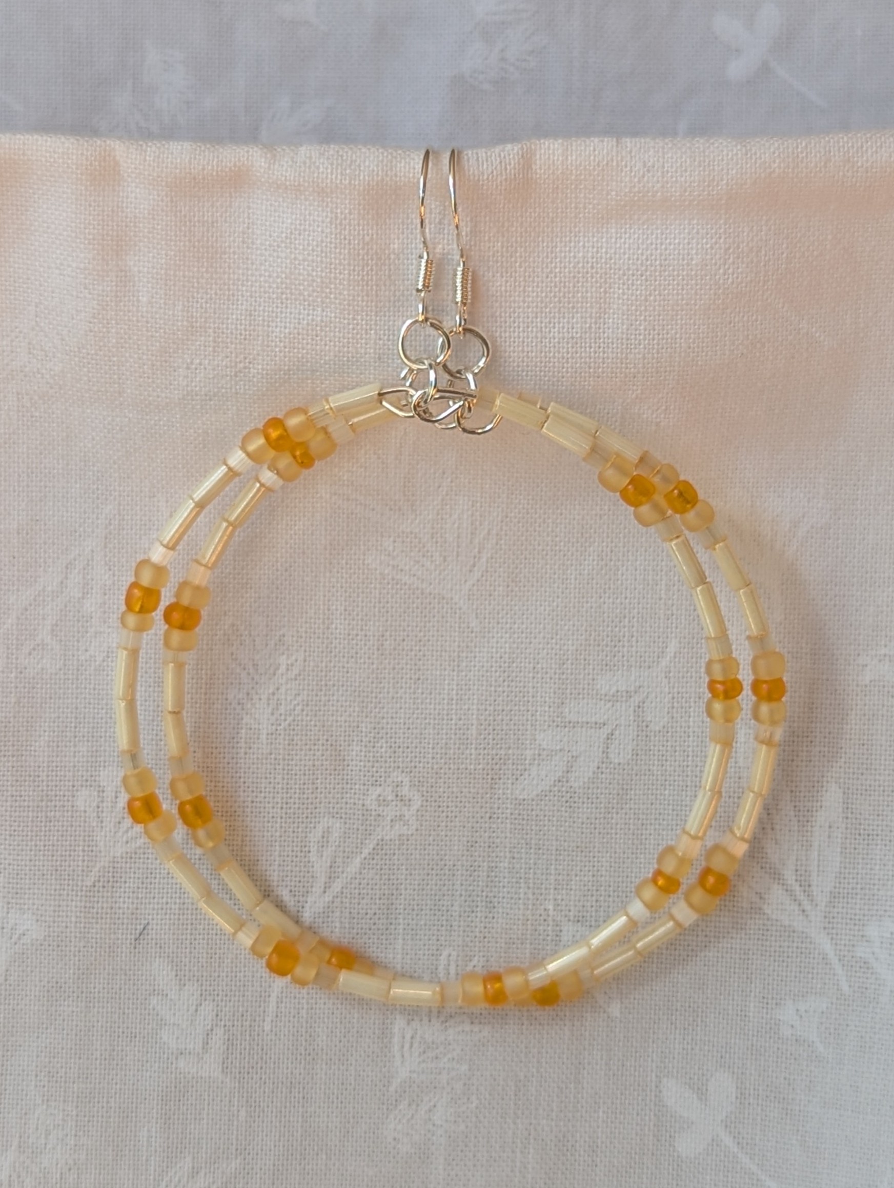 Handmade cream and sunshine yellow/orange beaded hoop earrings with glass beads on silver-plated memory wire and sterling silver hooks.