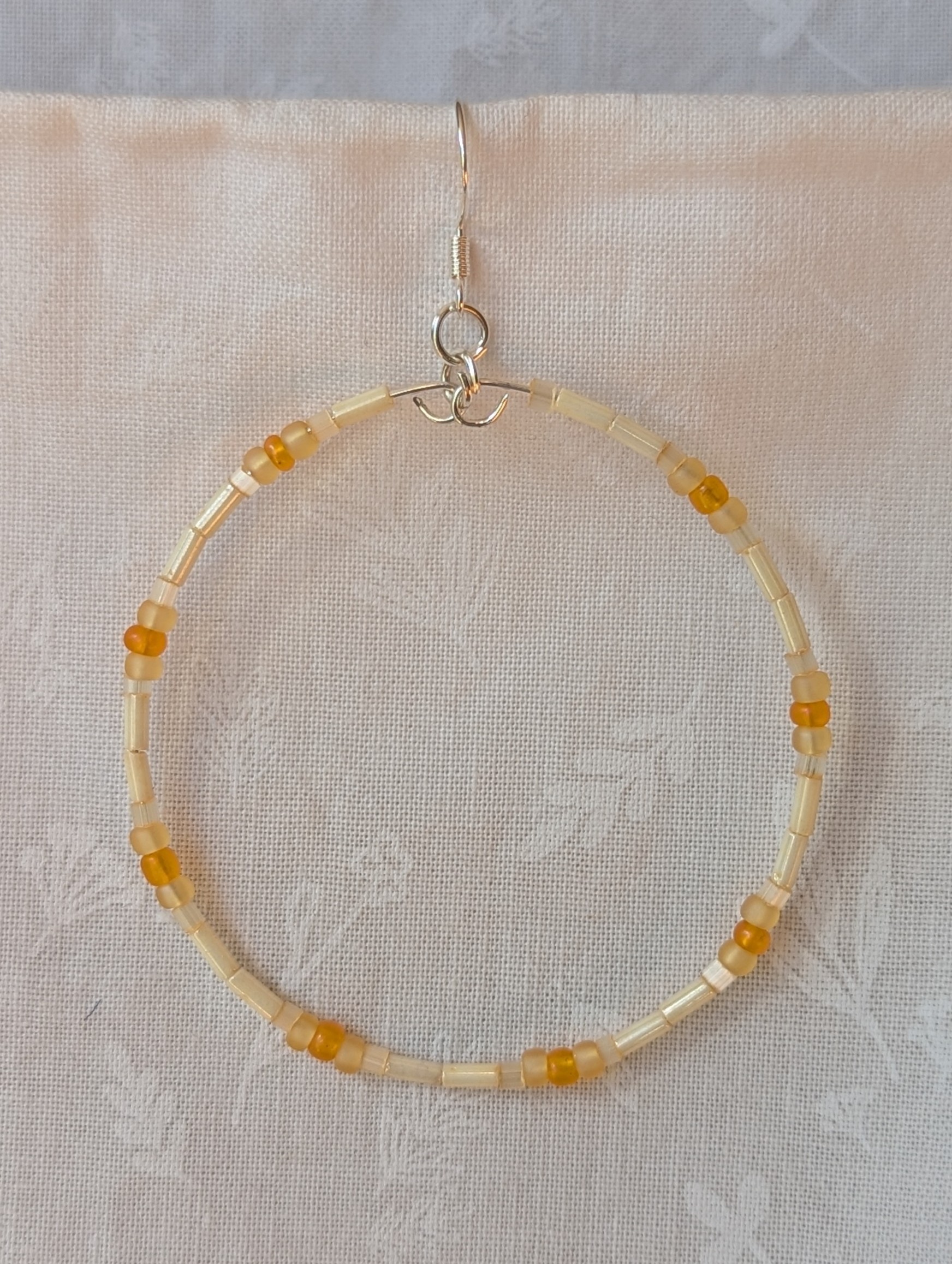 Handmade cream and sunshine yellow/orange beaded hoop earrings with glass beads on silver-plated memory wire and sterling silver hooks.