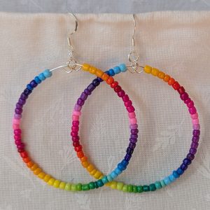 Handmade rainbow hoop earrings with glass seed beads in a full-color gradient on silver-plated memory wire and sterling silver hooks.