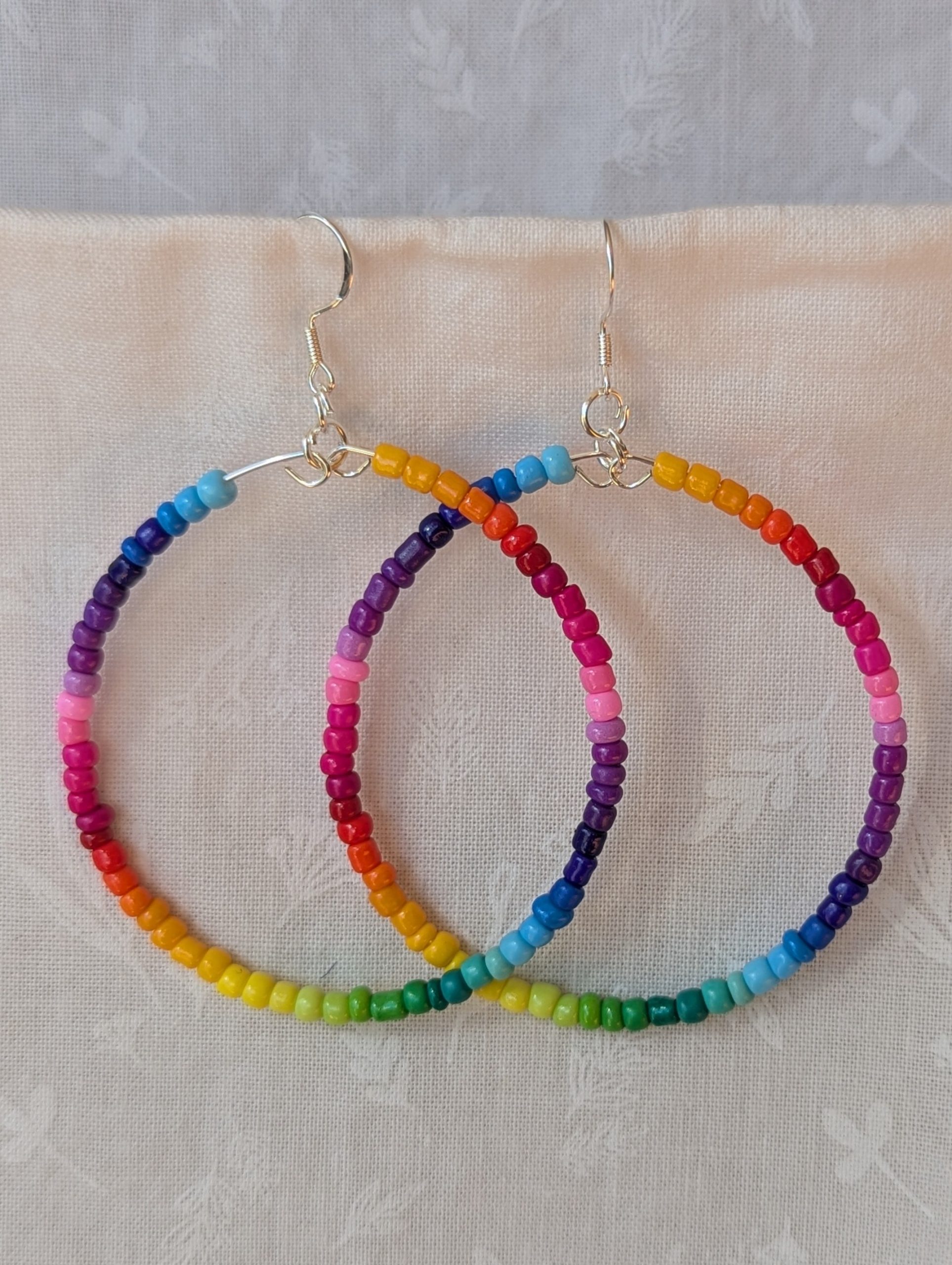 Handmade rainbow hoop earrings with glass seed beads in a full-color gradient on silver-plated memory wire and sterling silver hooks.