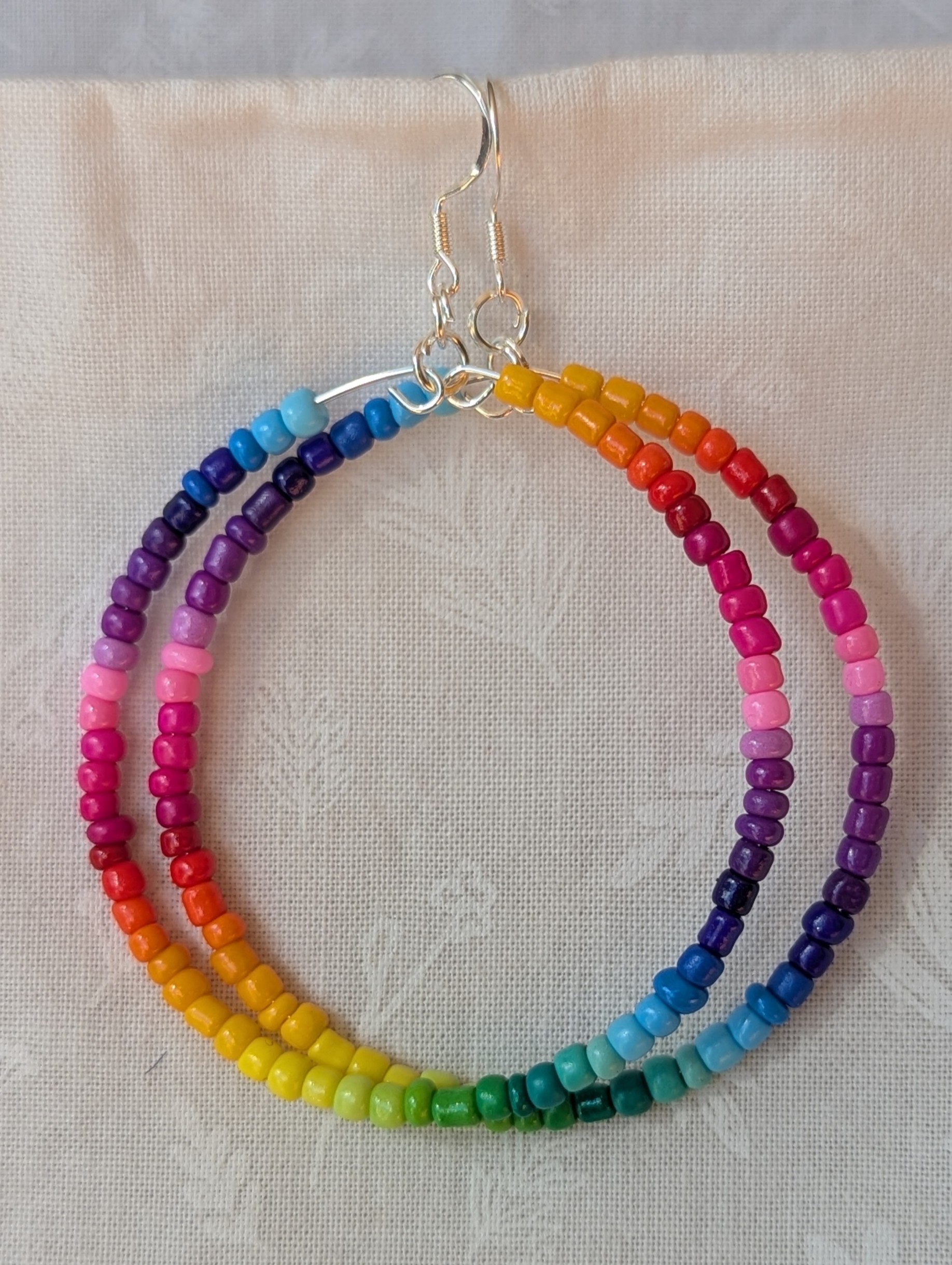 Handmade rainbow hoop earrings with glass seed beads in a full-color gradient on silver-plated memory wire and sterling silver hooks.
