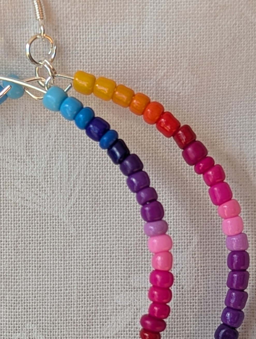 Handmade rainbow hoop earrings with glass seed beads in a full-color gradient on silver-plated memory wire and sterling silver hooks.