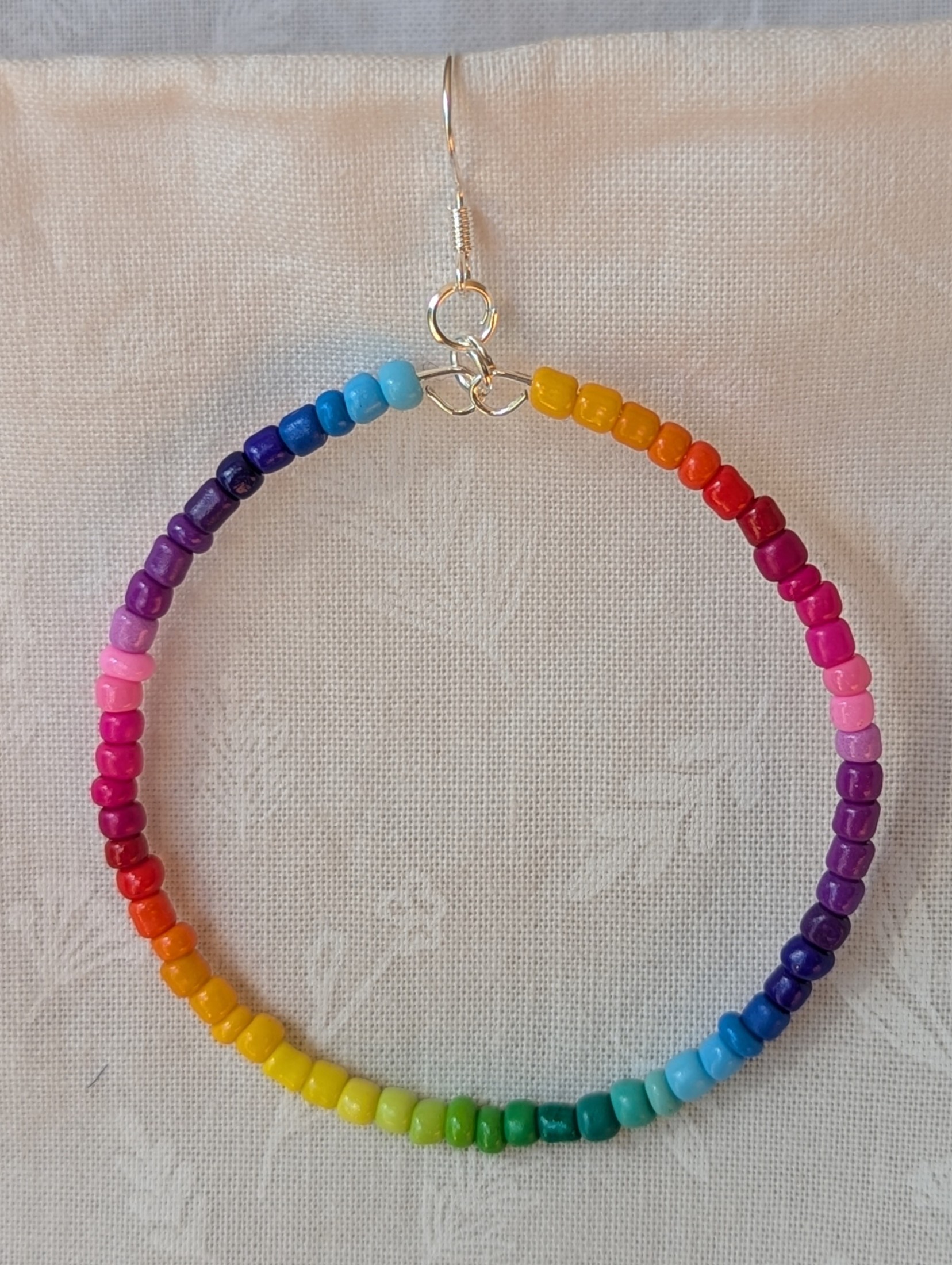 Handmade rainbow hoop earrings with glass seed beads in a full-color gradient on silver-plated memory wire and sterling silver hooks.