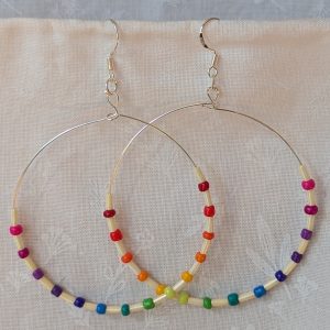 Handmade rainbow and cream accent hoop earrings with alternating colorful glass seed beads and long cream beads on silver-plated wire with sterling silver hooks.